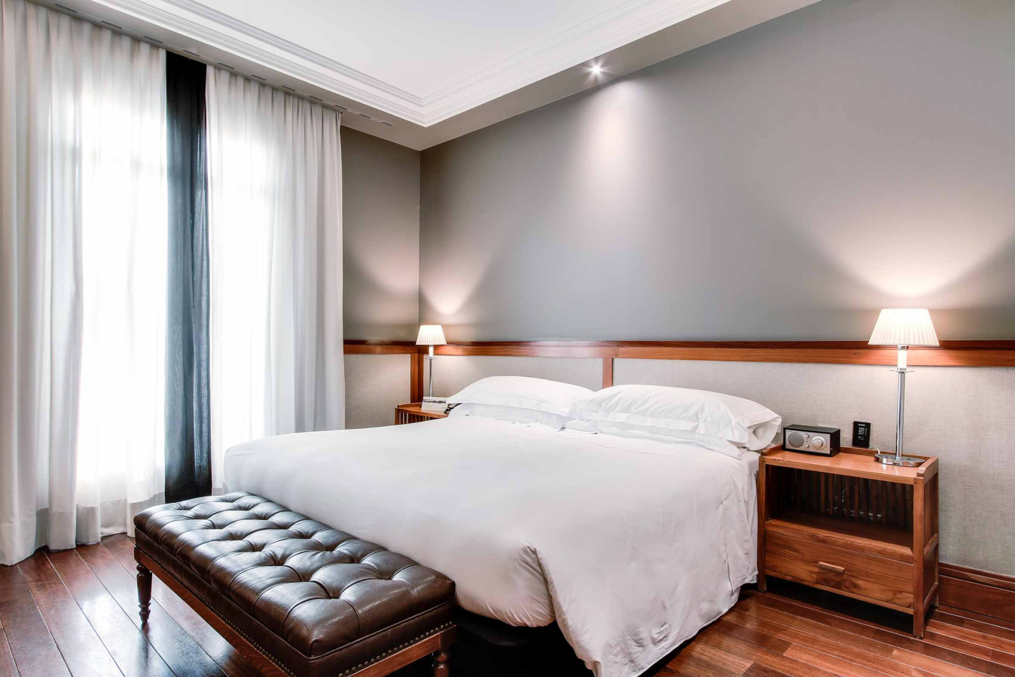 Describe una habitación con cama doble, mesita de noche y cortinas junto a una ventana.
