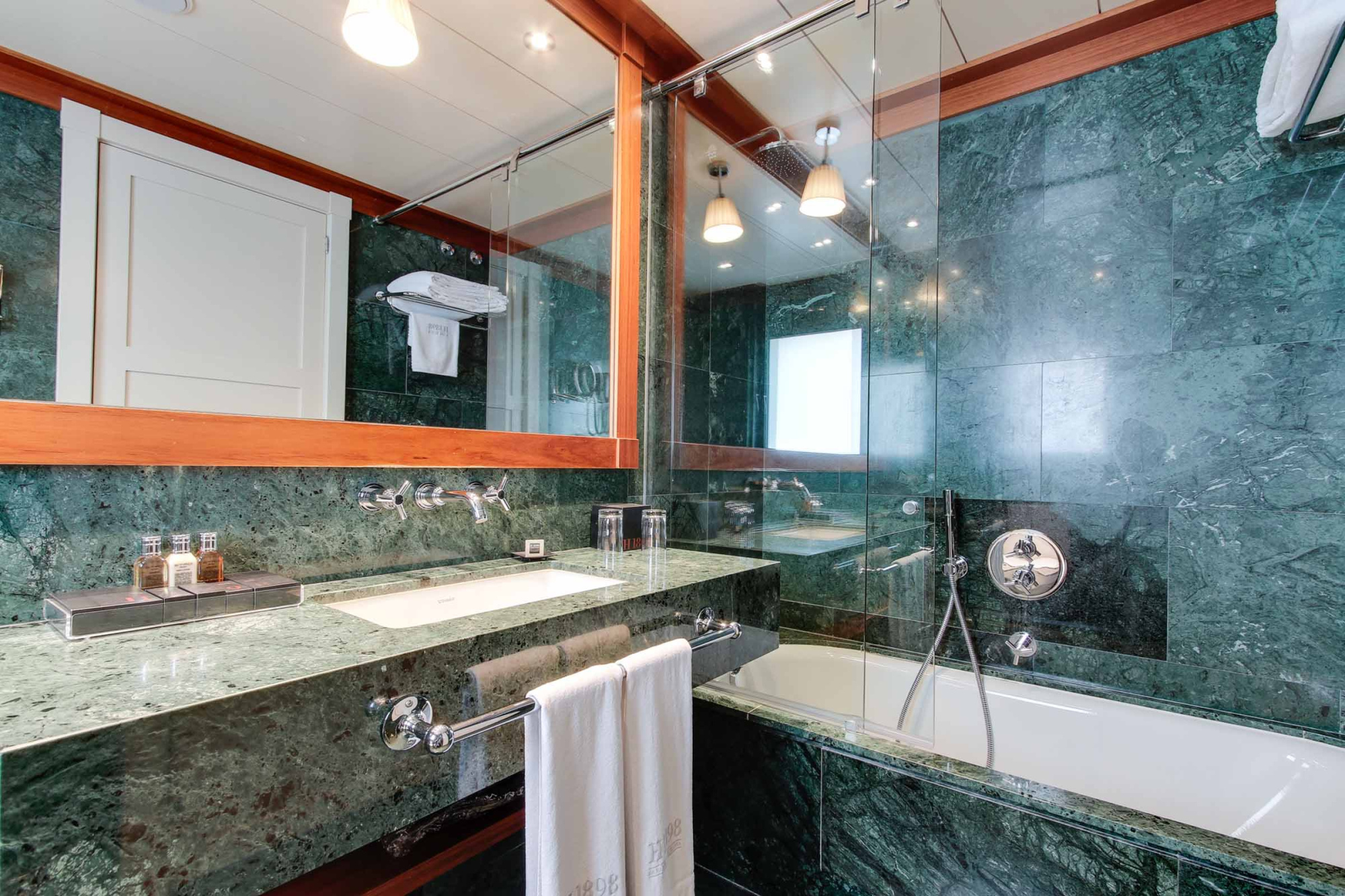 El baño muestra una bañera, un lavabo doble con encimera de piedra y una ducha con mampara de vidrio.