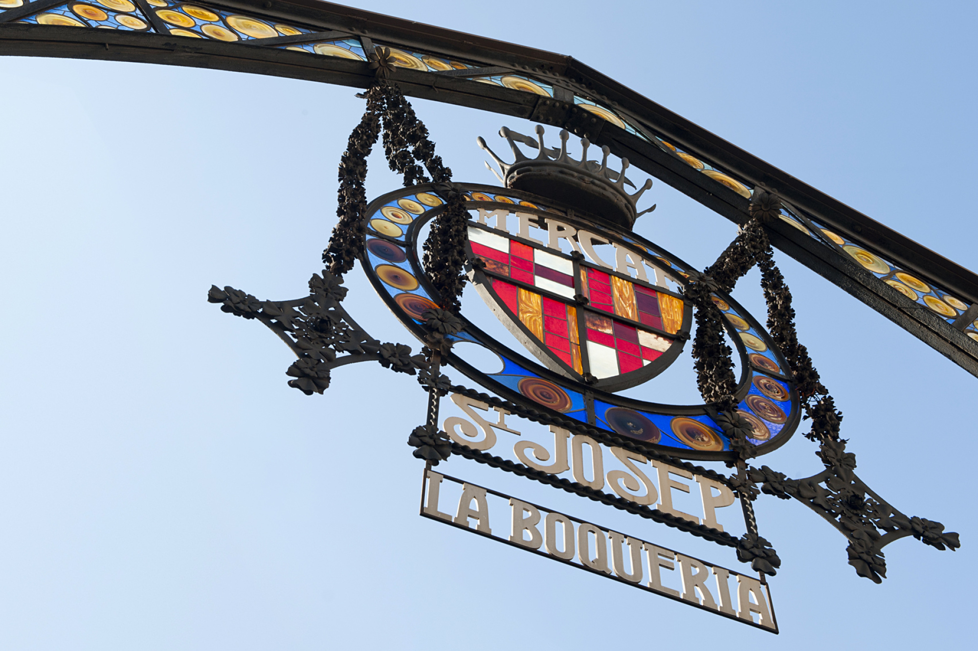 Se ve un letrero de La Boqueria con un emblema circular sobre una estructura metálica.