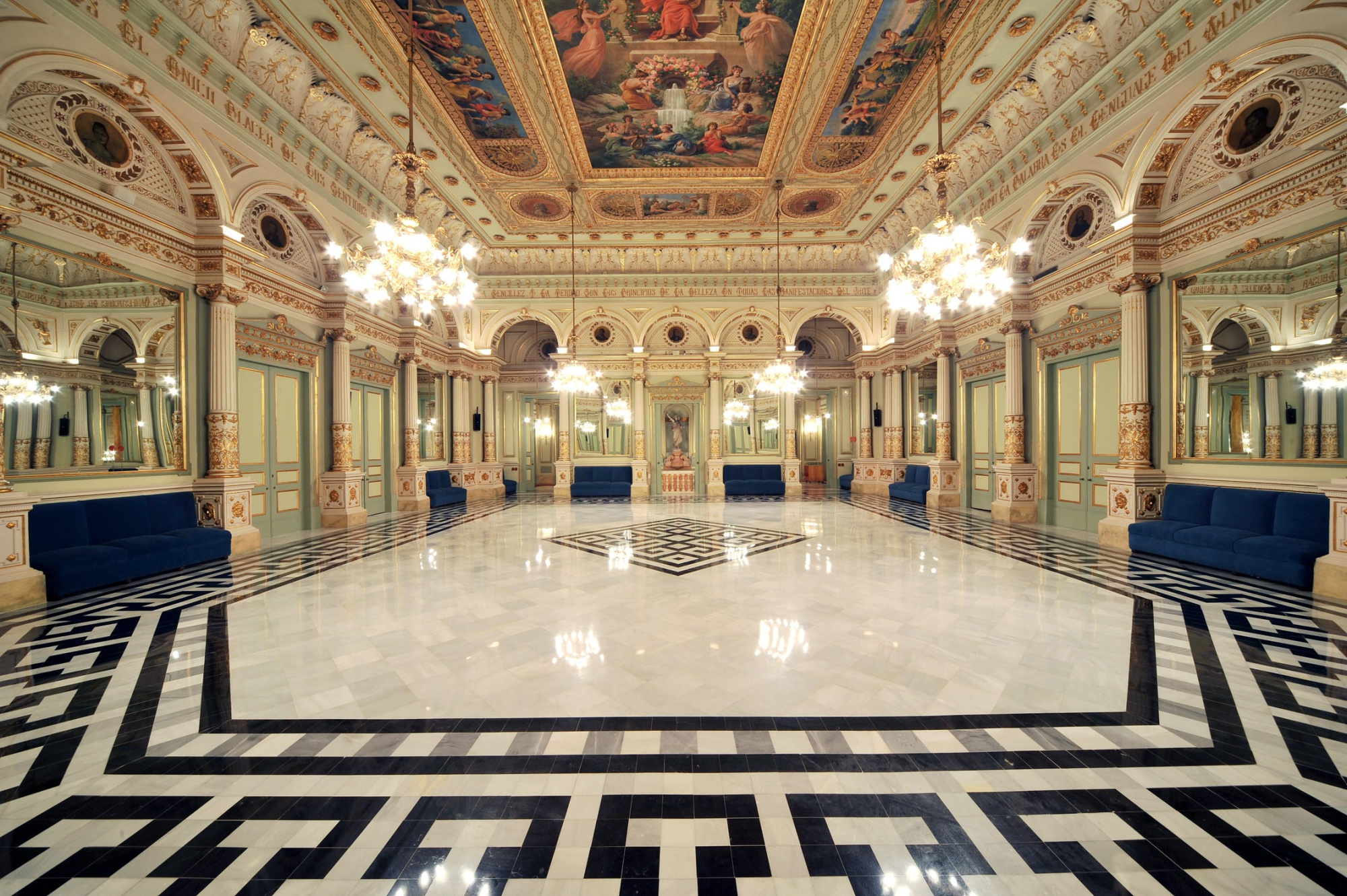Se ve un salón amplio con suelo de mármol, lámparas de techo y paredes con arcos decorativos.
