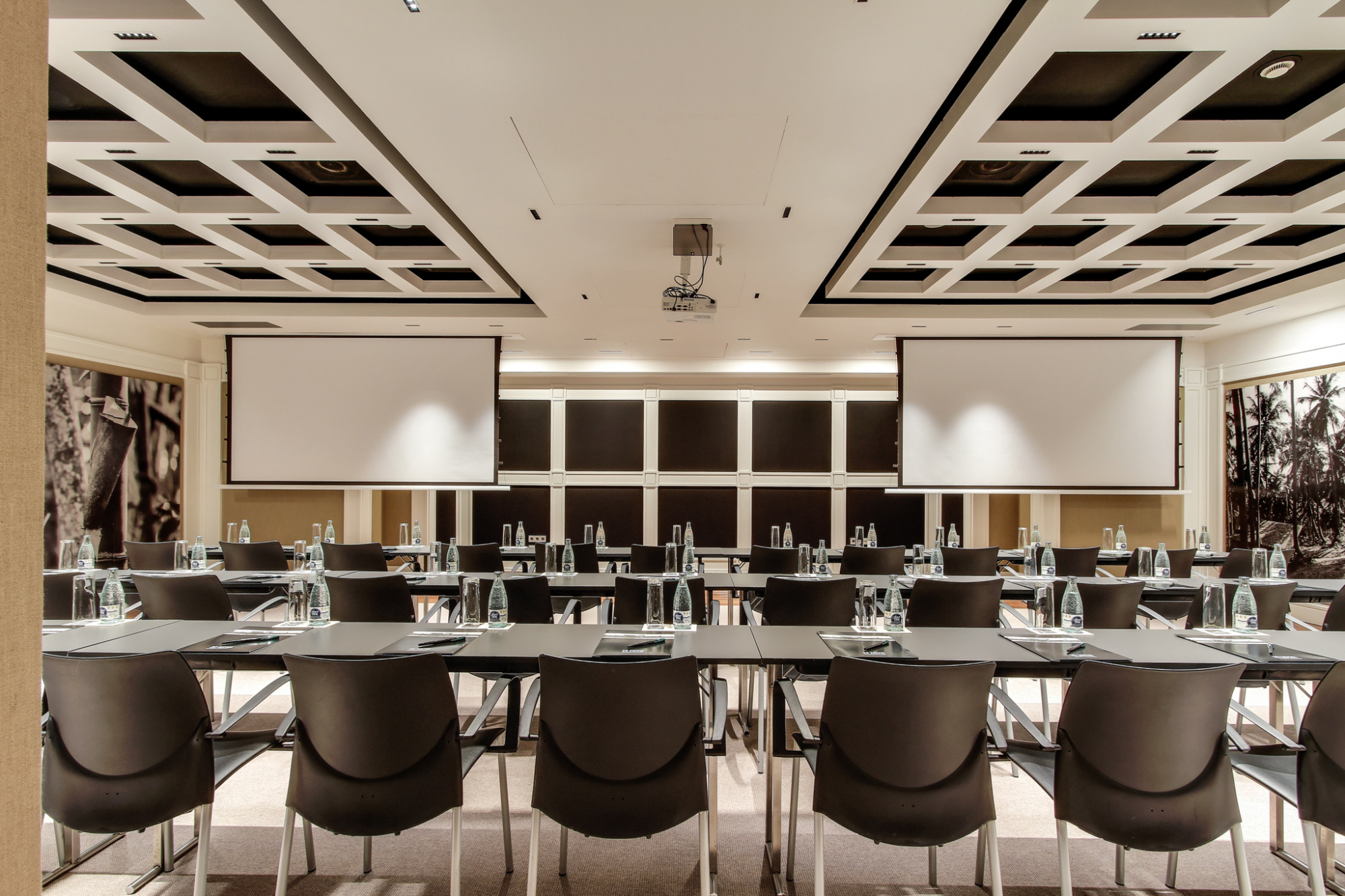 La sala de reuniones muestra mesas con sillas y una pared con paneles y pantallas.