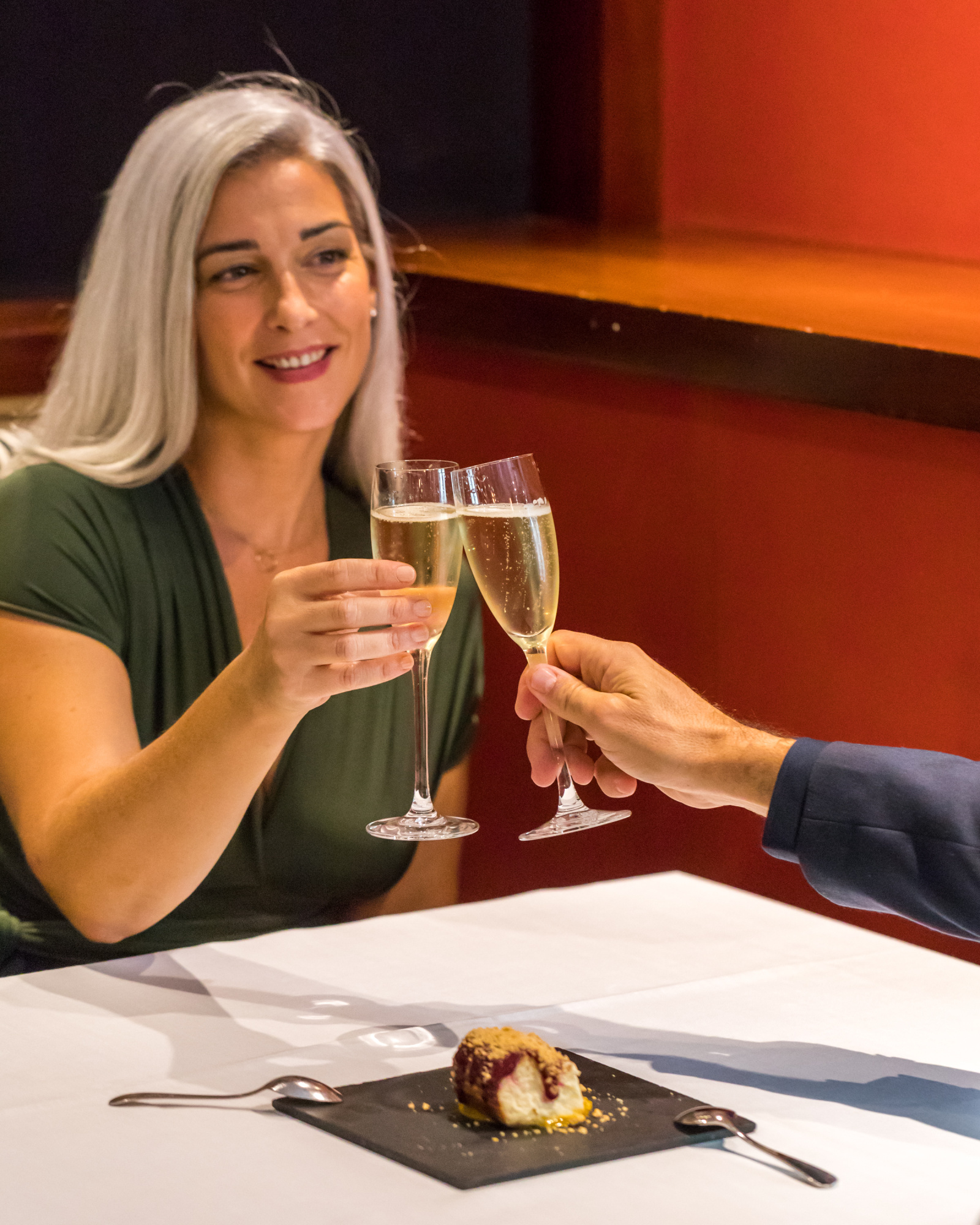 Dos personas brindan con copas de champán sobre una mesa con un plato servido.