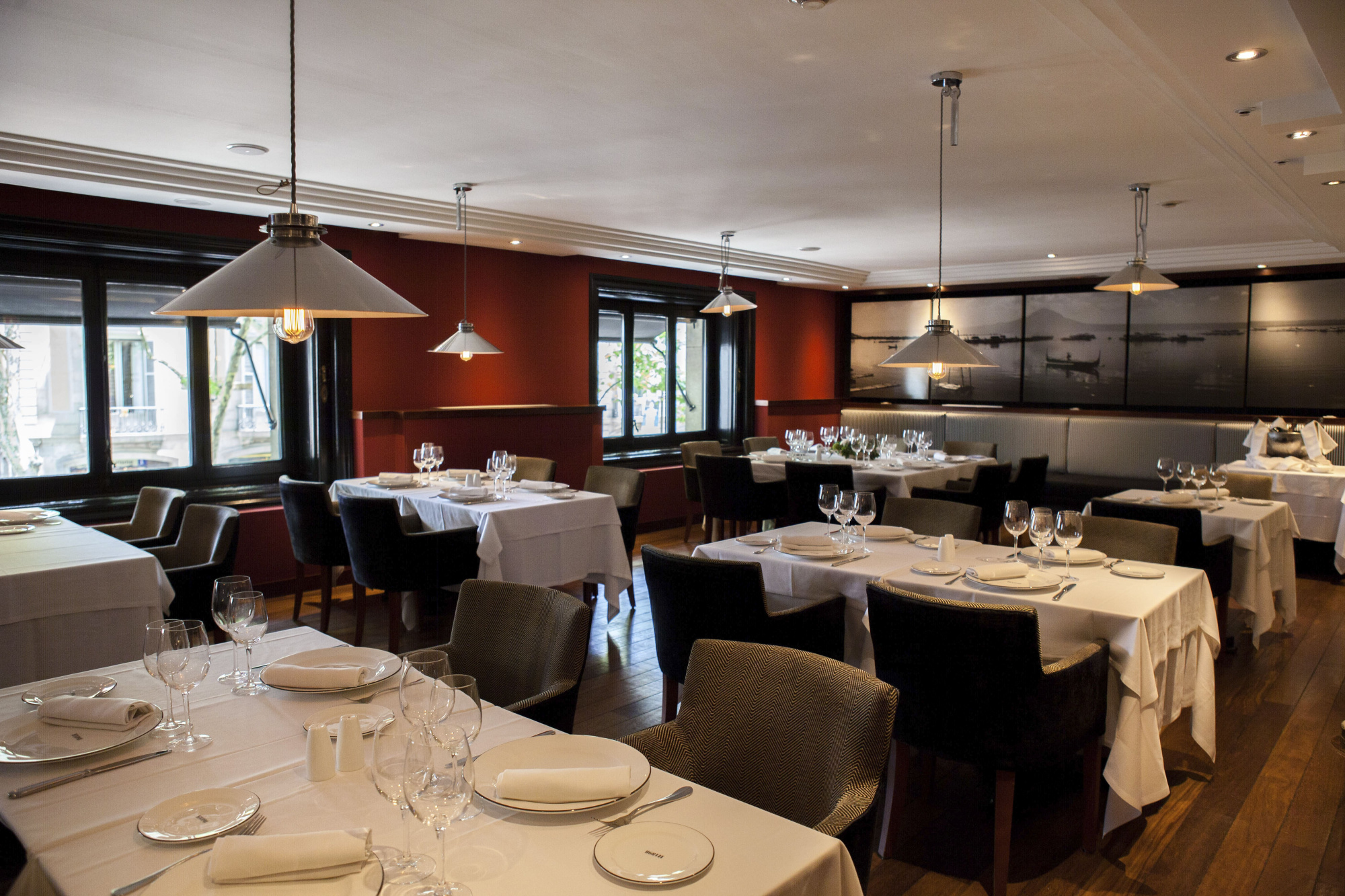 El restaurante muestra mesas con manteles blancos, vajilla y copas, junto a asientos tapizados y lámparas colgantes.