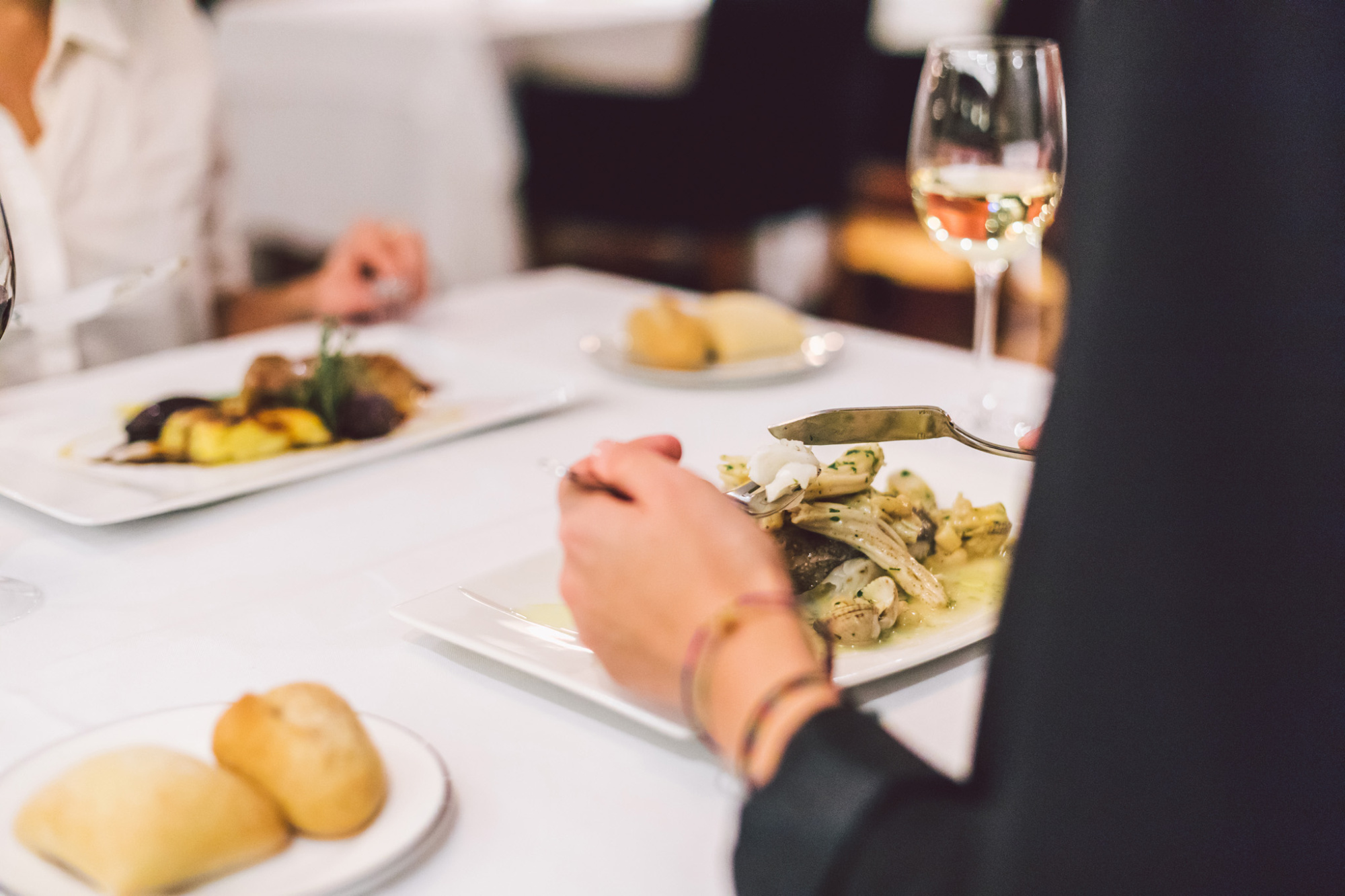 Se ve una mesa de restaurante con platos servidos y una copa de vino sobre el mantel.