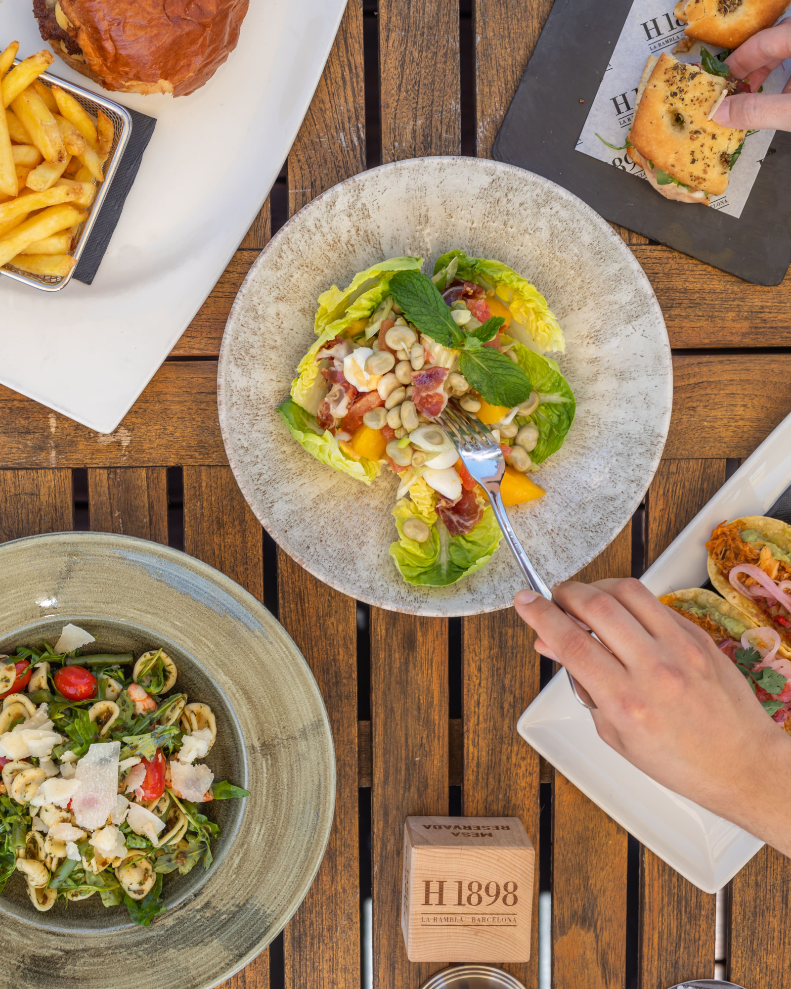 Se ven varios platos servidos sobre una mesa de madera con cubiertos y comida preparada.