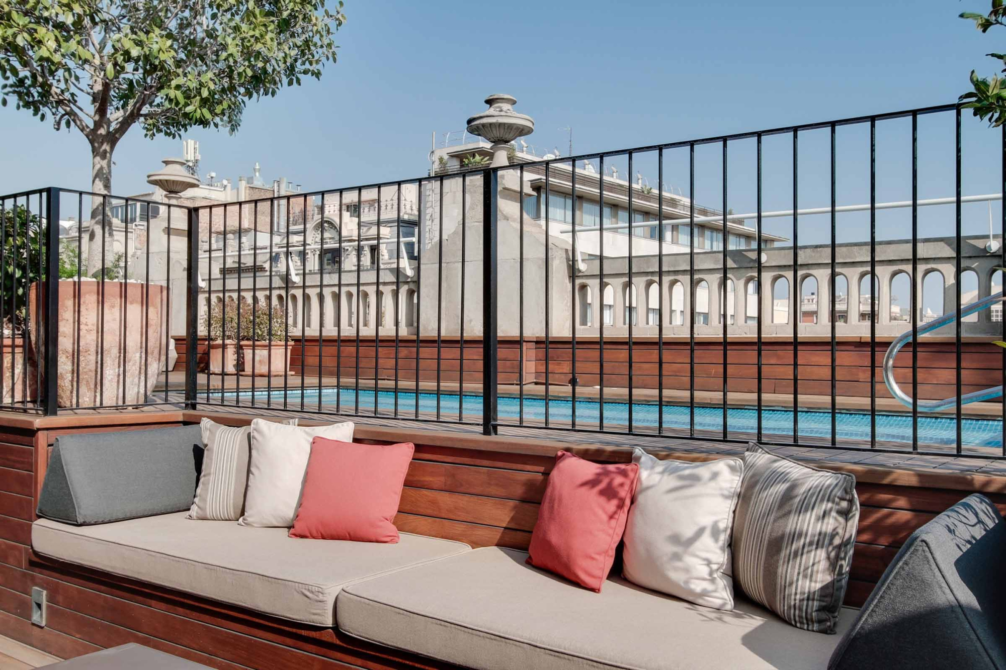 Se ve una terraza con un sofá con cojines y una piscina detrás de una barandilla de metal.