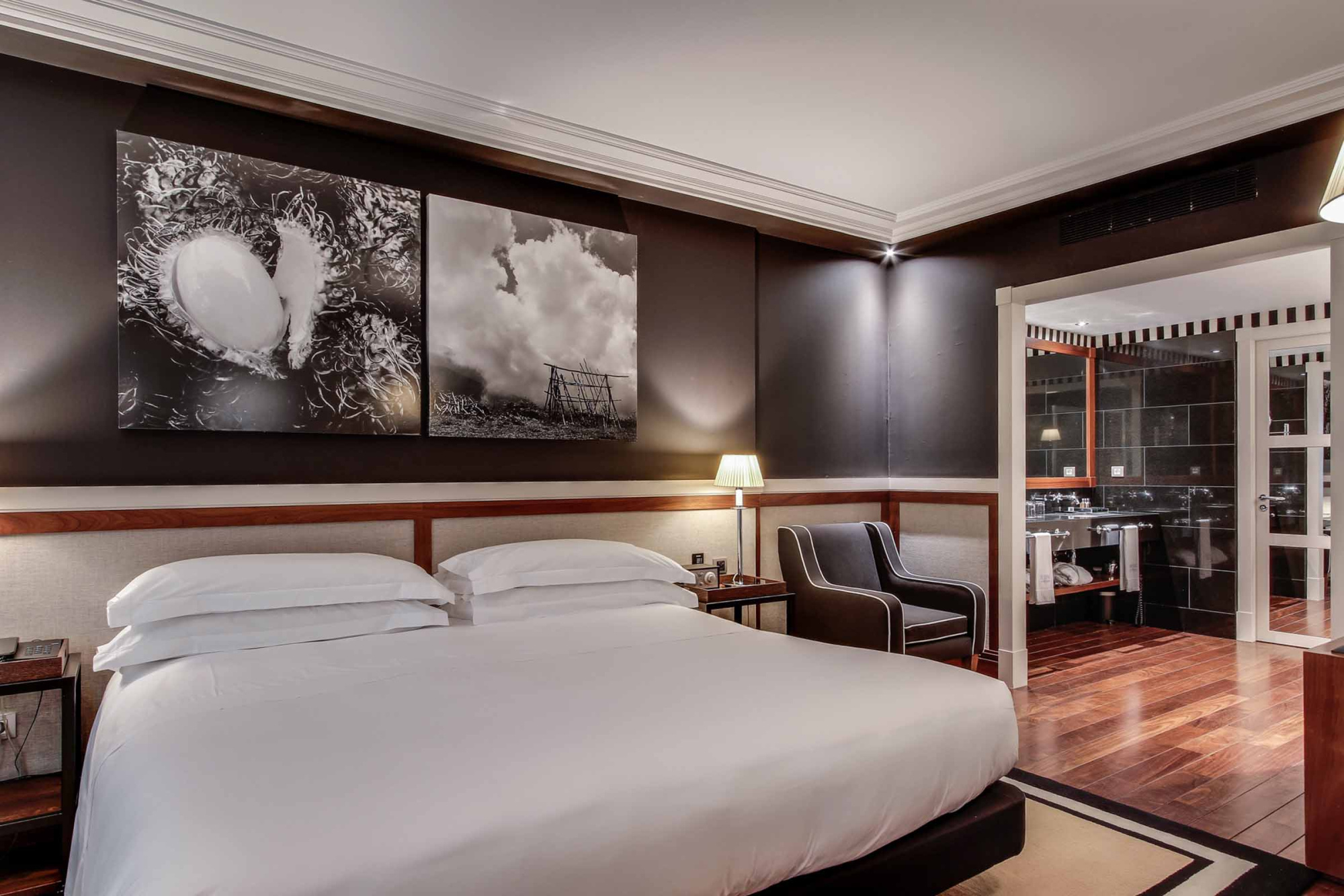 La imagen muestra una suite con cama doble, cabecero de madera y una zona de bar con vitrina al fondo.