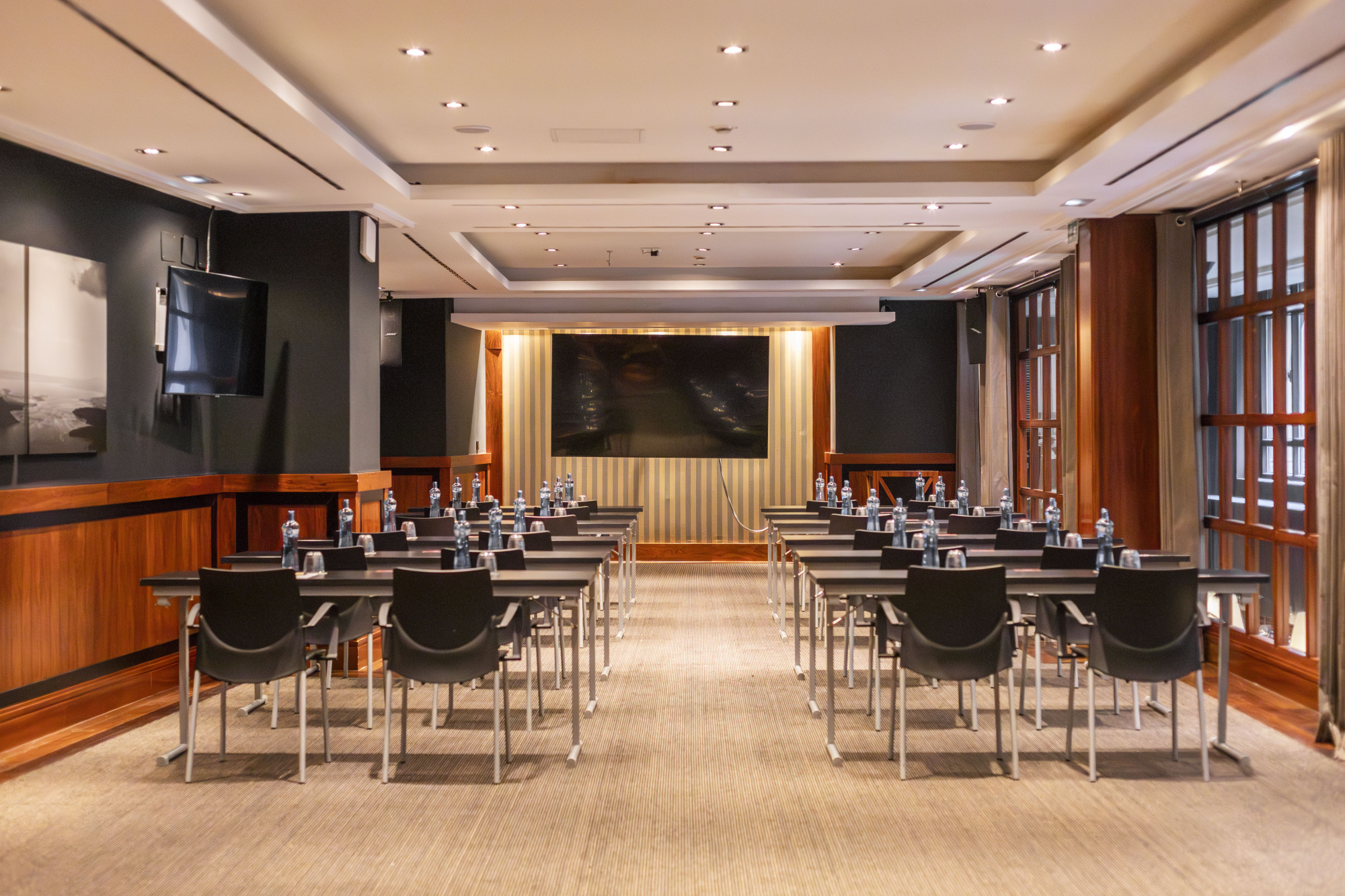 Sala de reuniones con mesas y sillas alineadas, iluminación empotrada y paneles de madera.