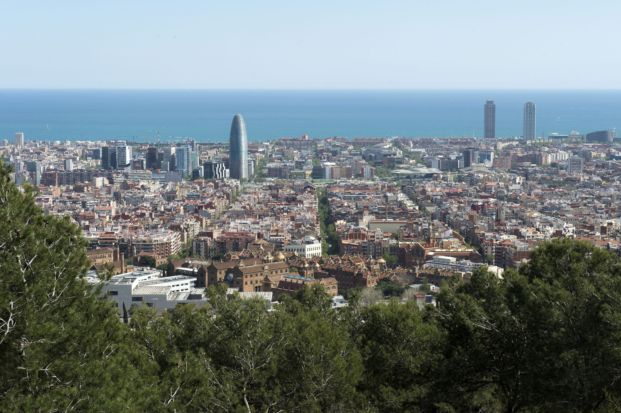Se ve un panorama urbano de Barcelona con el mar al fondo.