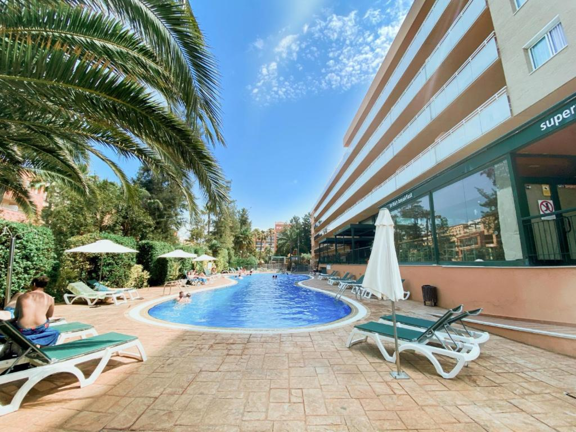 Una piscina al aire libre con tumbonas blancas y un edificio en el fondo, en un entorno de vacaciones en Salou.