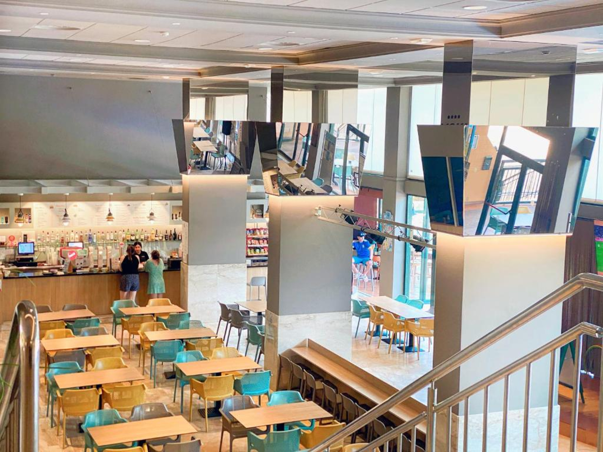 Imagen de un restaurante en Aparthotel SunClub Salou, con mesas y sillas, y personas en el fondo, creando un ambiente acogedor y social.