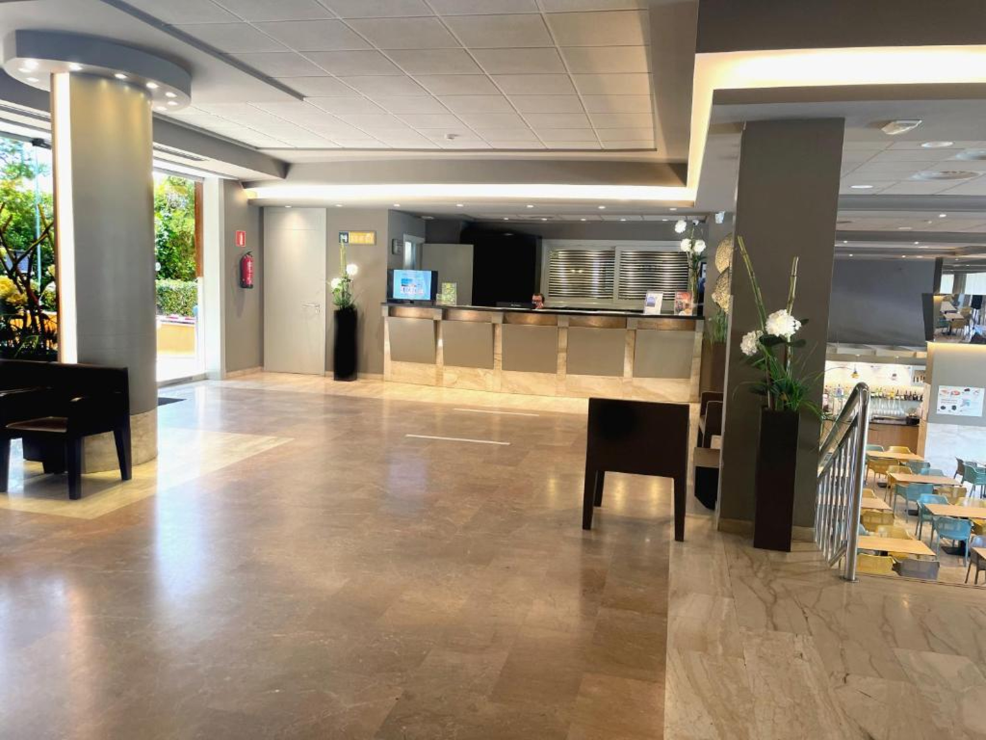 El vestíbulo presenta un área de espera con mesas y sillas, decorada en tonos neutros y con un ambiente acogedor, ideal para relajarse antes de acceder a las habitaciones.