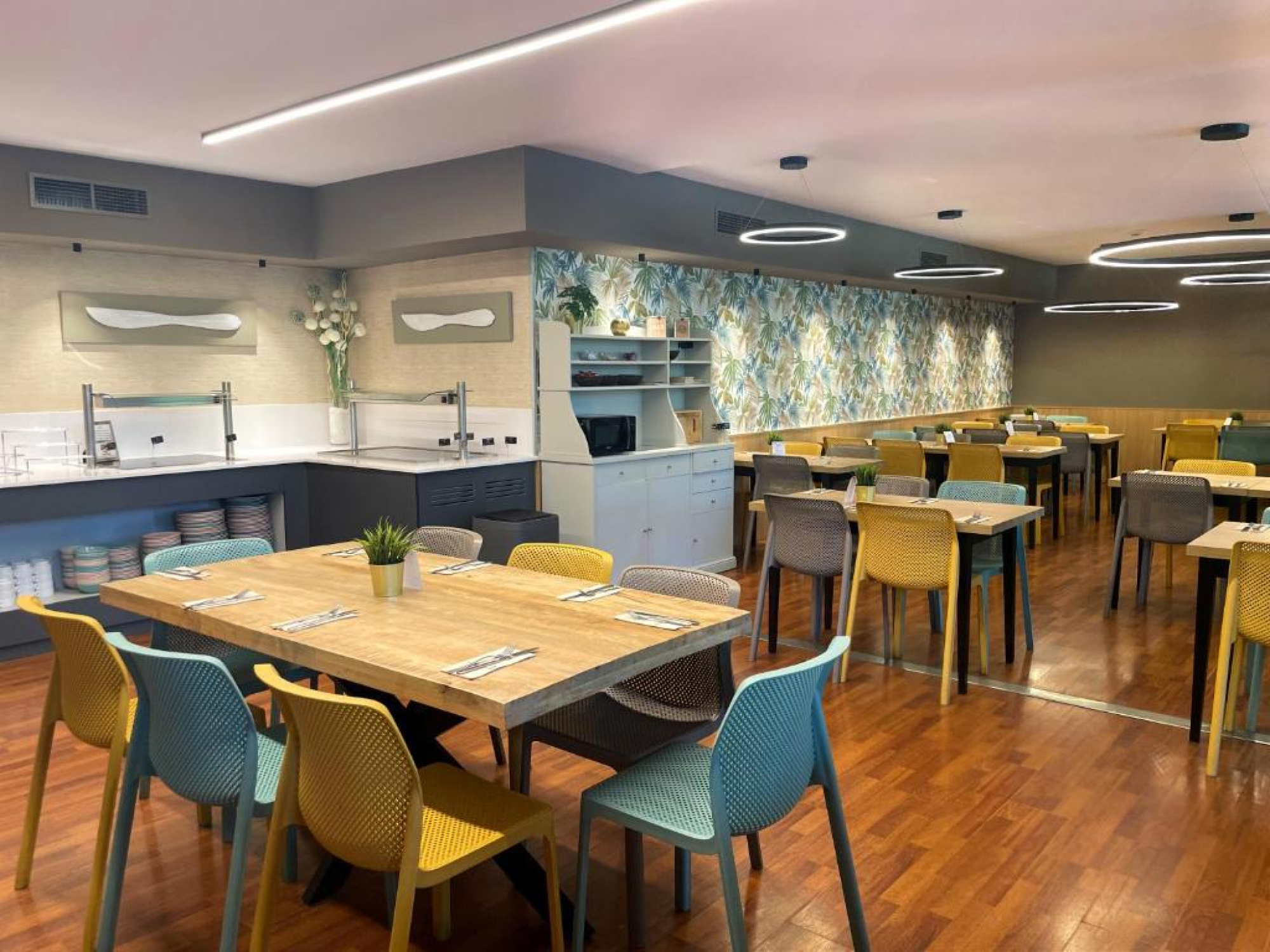 El restaurante presenta mesas y sillas en un ambiente luminoso y acogedor, con una cocina visible en el fondo que sugiere un espacio moderno y bien equipado para los huéspedes.
