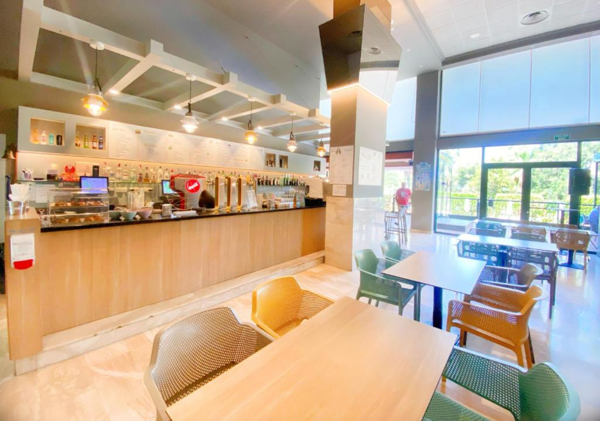 El restaurante presenta mesas y sillas modernas en un ambiente luminoso y acogedor, con un mostrador en el fondo. Es un espacio diseñado para ofrecer comodidad y estilo a los huéspedes.