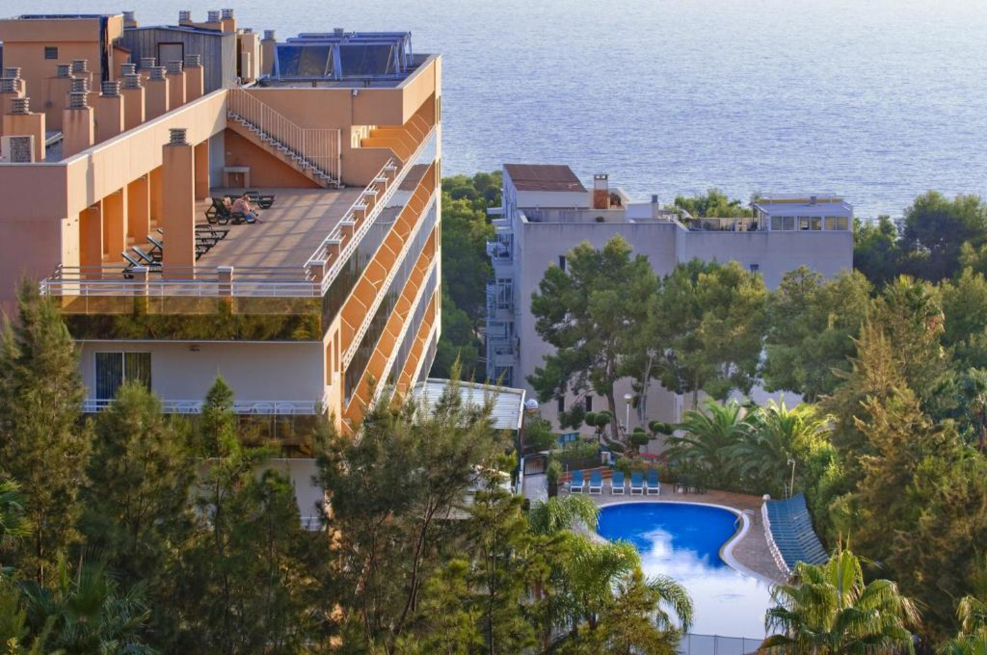 Una vista panorámica de un resort con una piscina grande y áreas de descanso, rodeado de vegetación y edificios residenciales en el fondo, en un entorno de vacaciones en Salou.