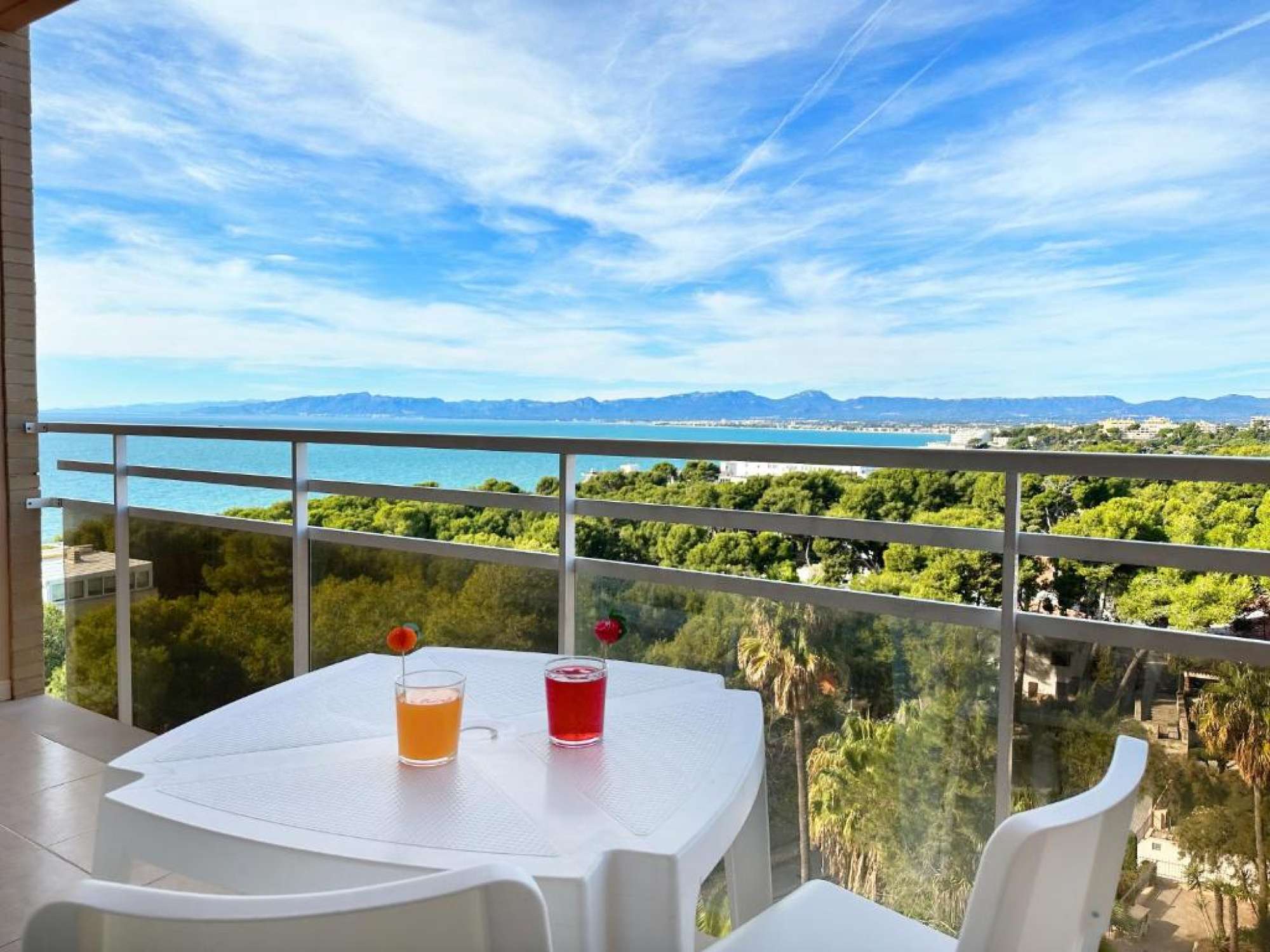 Dos bebidas en vasos altos sobre una mesa blanca en un balcón, con vista a un entorno exterior en SunClub Salou, creando un ambiente relajante y agradable para los huéspedes.