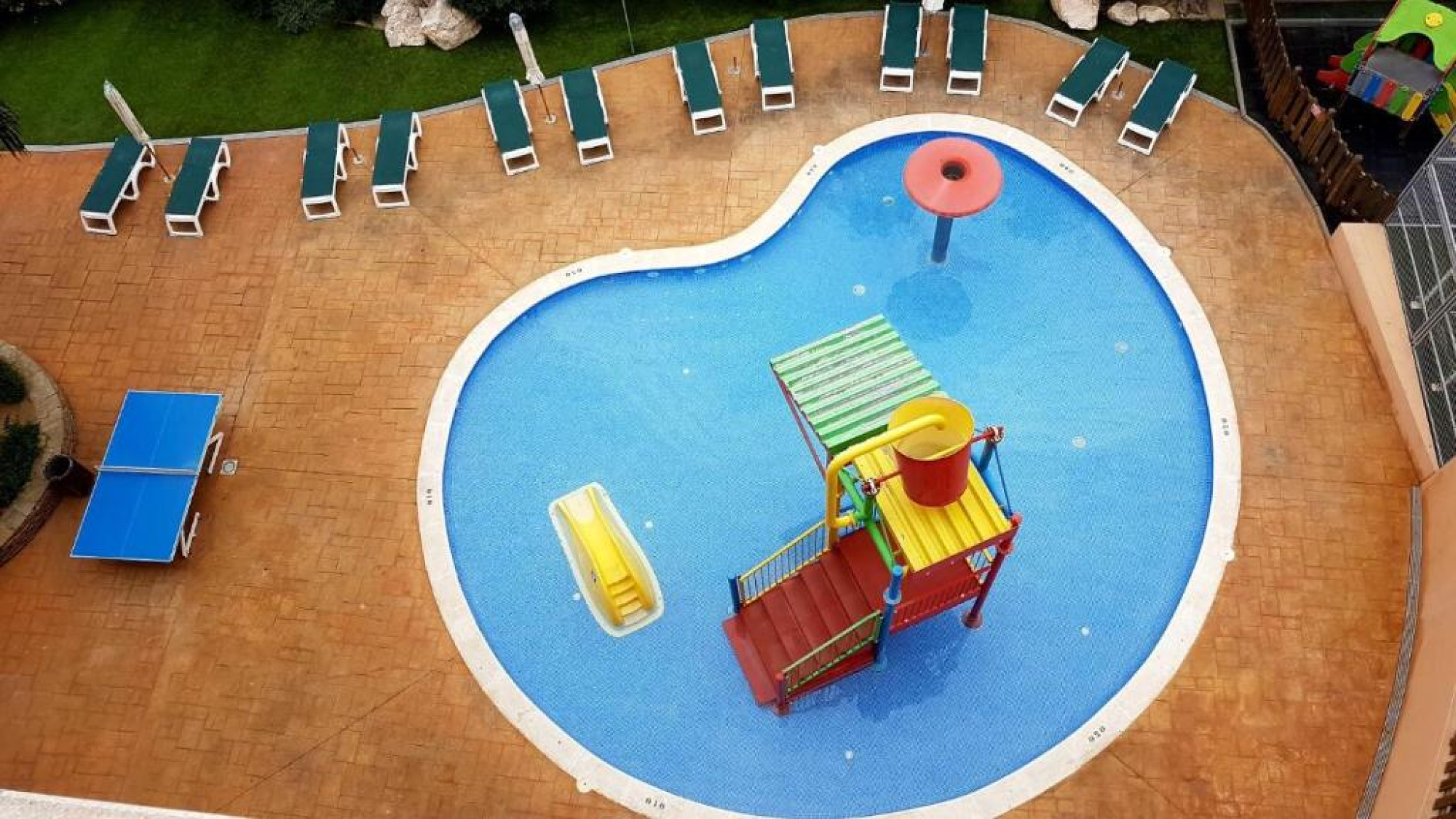 Vista aérea de una piscina de juguete en el Aparthotel SunClub Salou, diseñada para el entretenimiento infantil, con agua clara y rodeada de áreas de descanso.