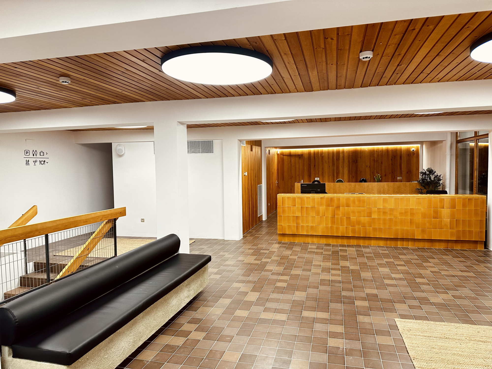 La imagen muestra una elegante área de recepción con un mostrador de madera clara y detalles decorativos en tonos neutros, creando un ambiente acogedor y moderno.