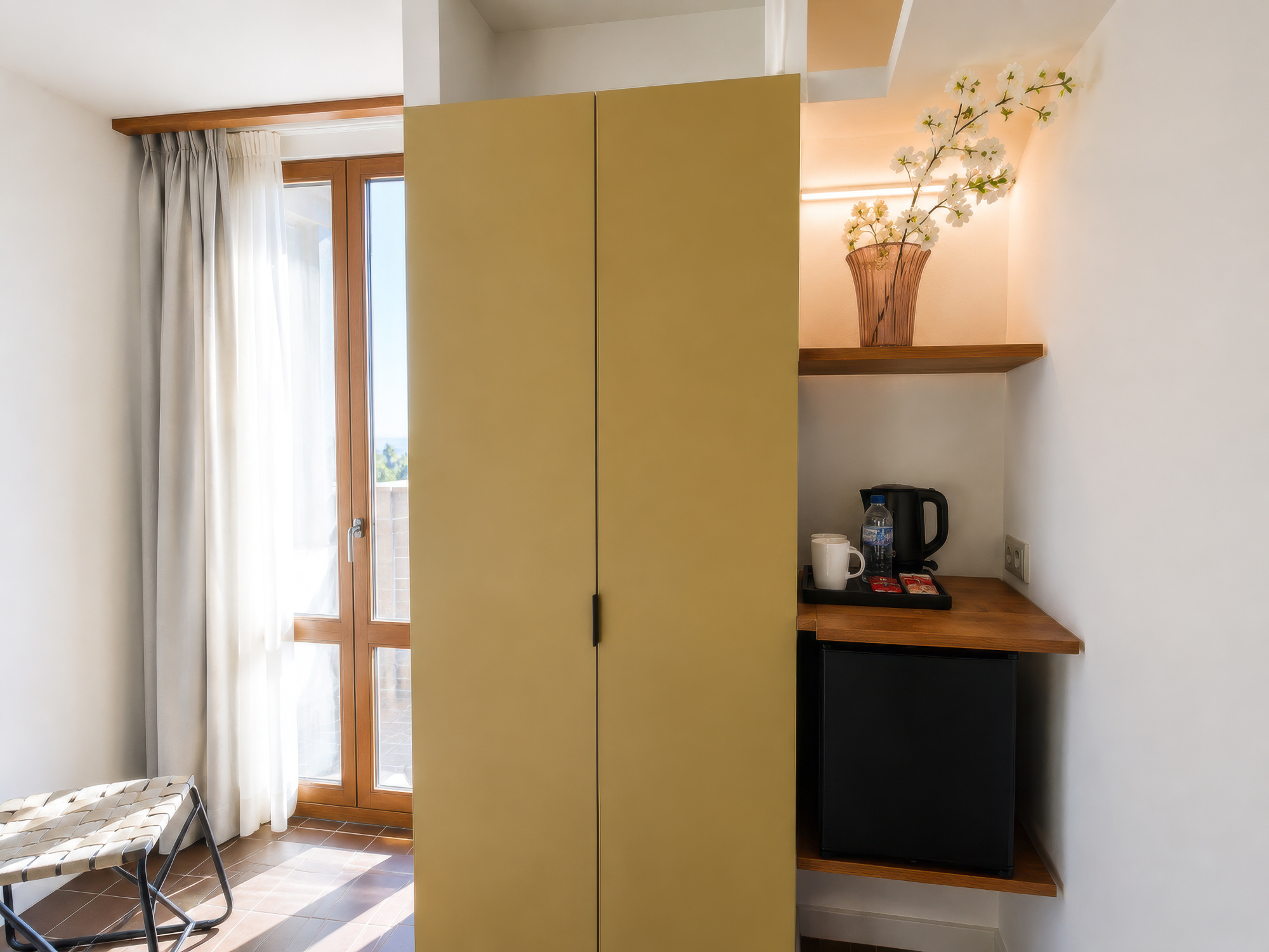 Se ve una zona de cocina con armario, encimera y cafetera junto a una puerta de acceso a un balcón y cortinas.
