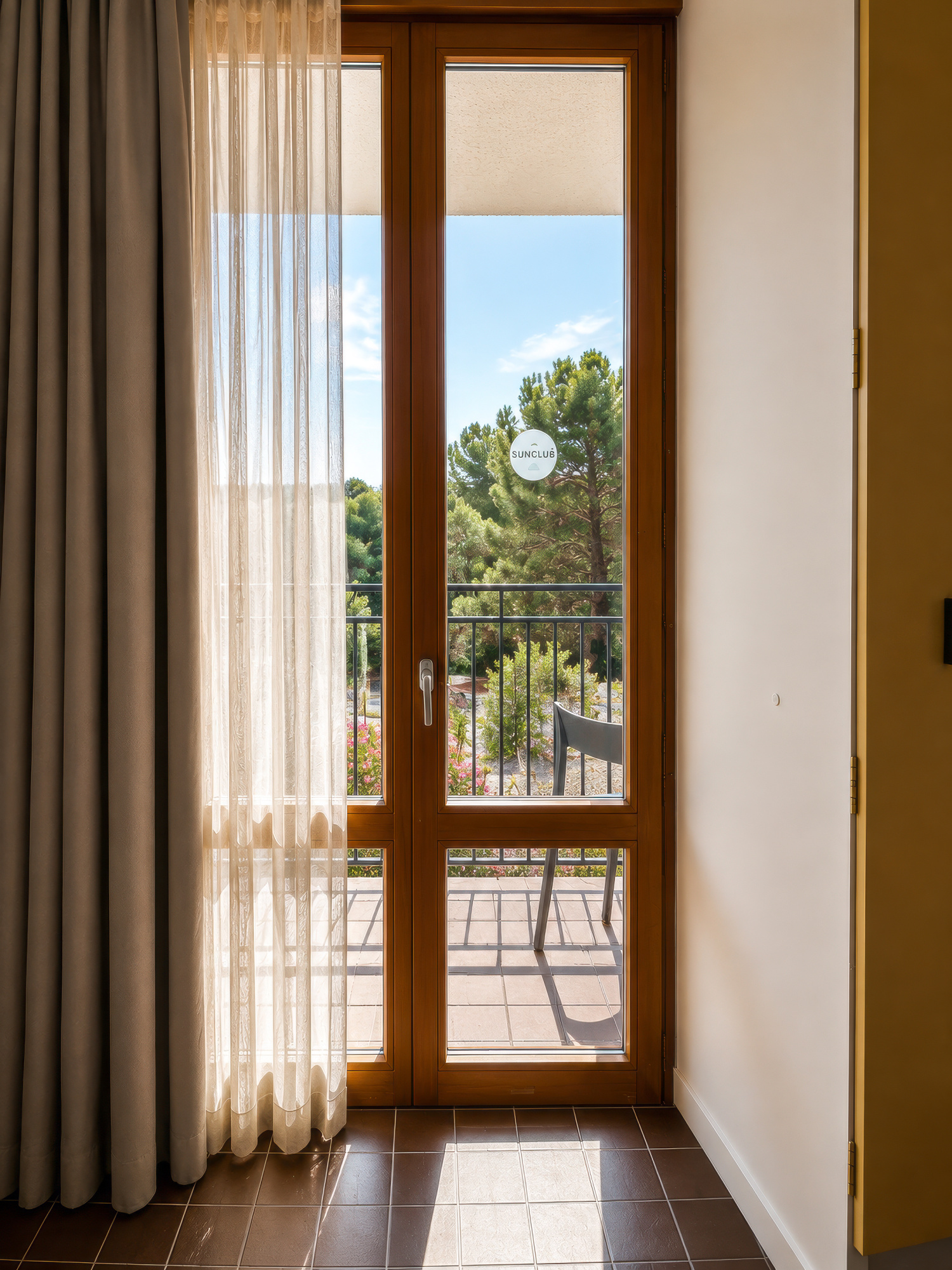 Se ve una puerta de madera abierta a una terraza con barandilla y luz del día al fondo.