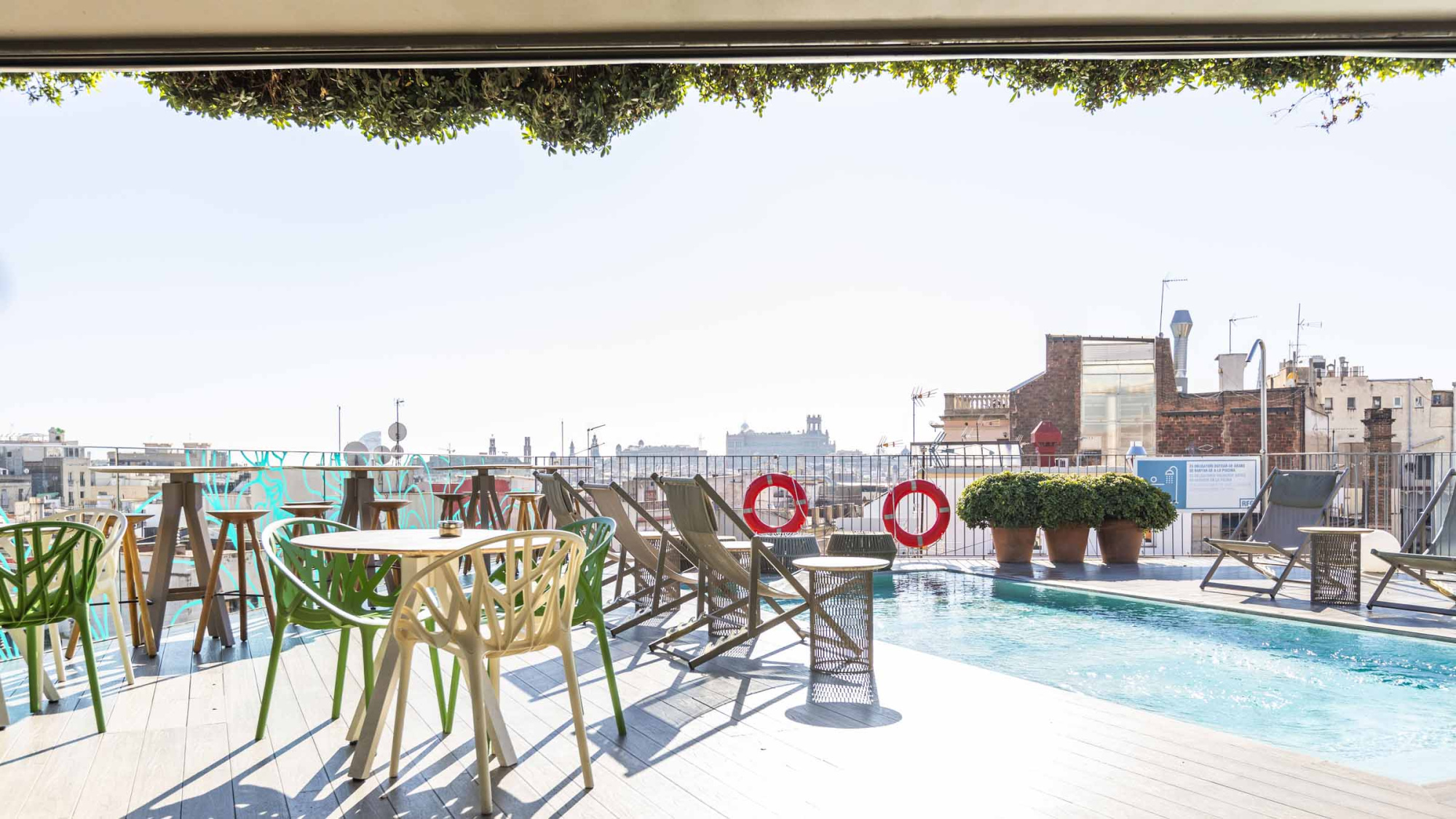 Se ve una terraza con sillas y una piscina al aire libre junto a una vista urbana.