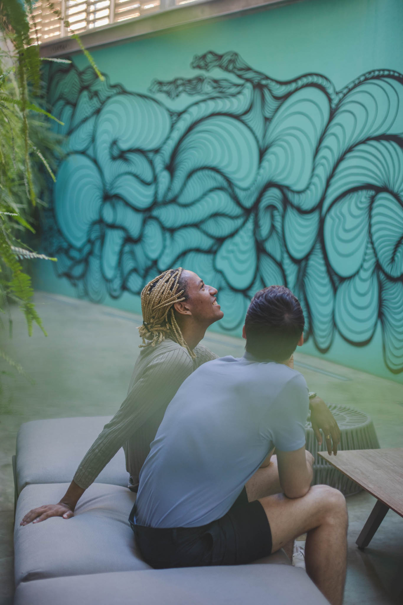 Dos personas se sientan en un sofá junto a un mural colorido en la pared.