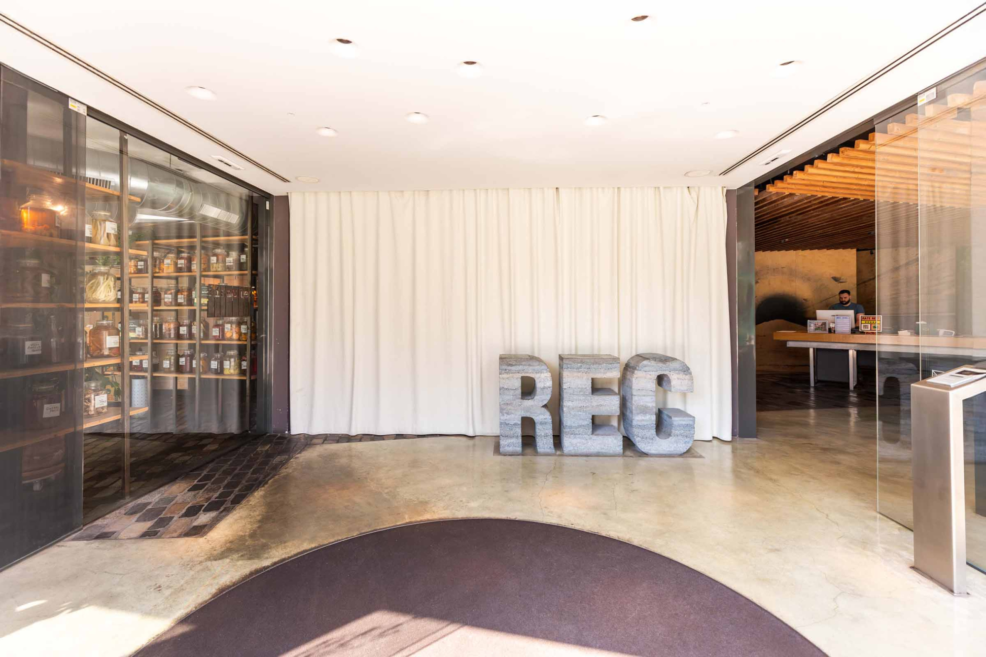 Se ve una zona de recepción con una vitrina de bebidas, una barra y un letrero REC en el suelo.
