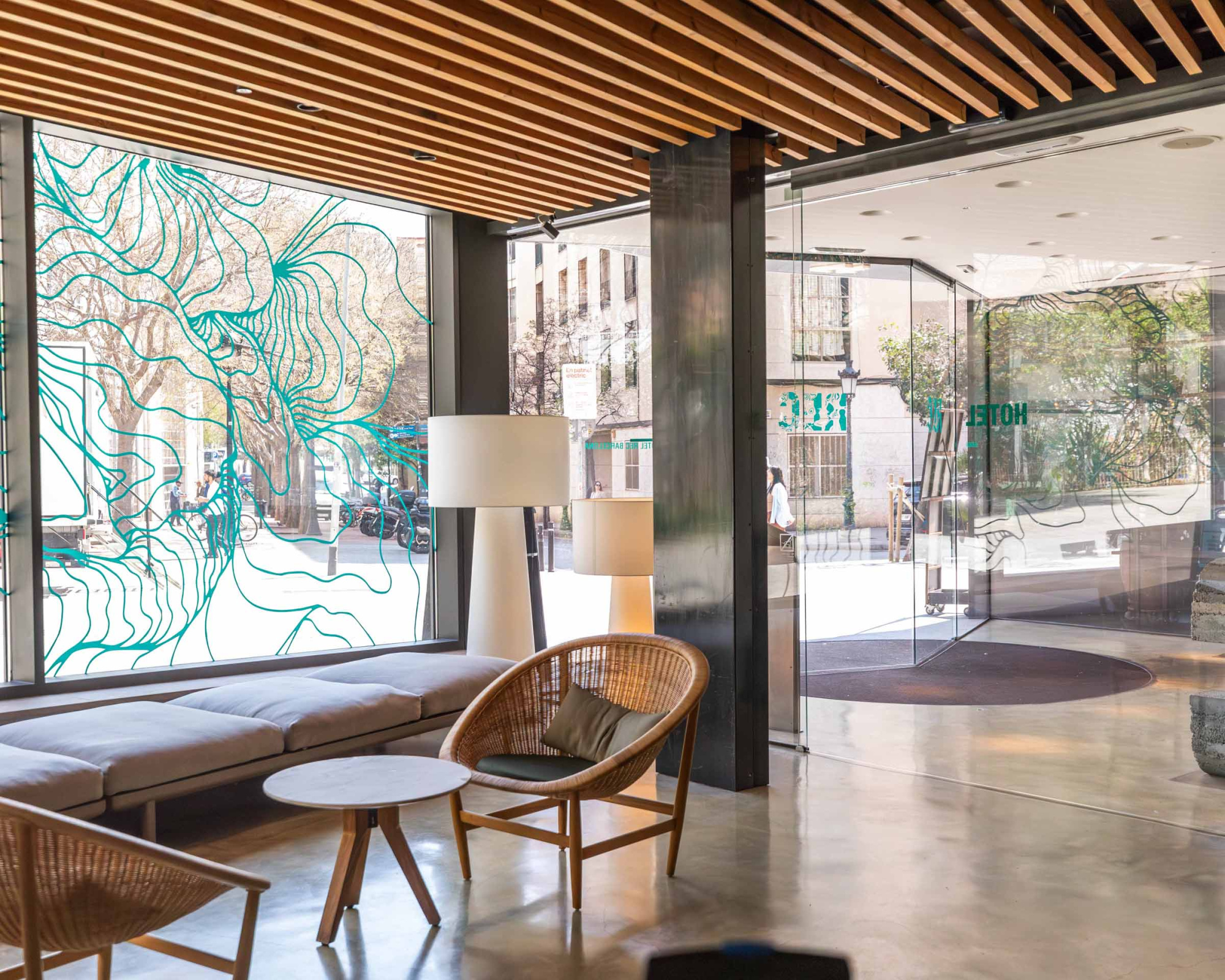 Lobby del hotel con sillones, mesas auxiliares y grandes ventanales de vidrio hacia el exterior.