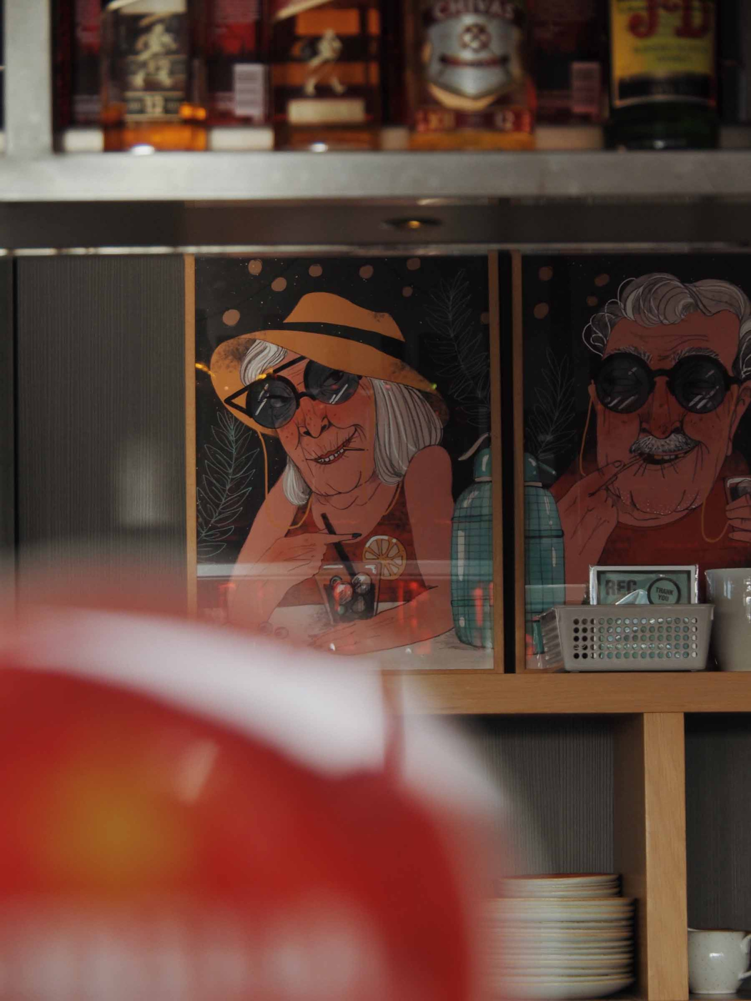 Se ve una barra de bar con botellas y vasos detrás, además de ilustraciones en el panel frontal.