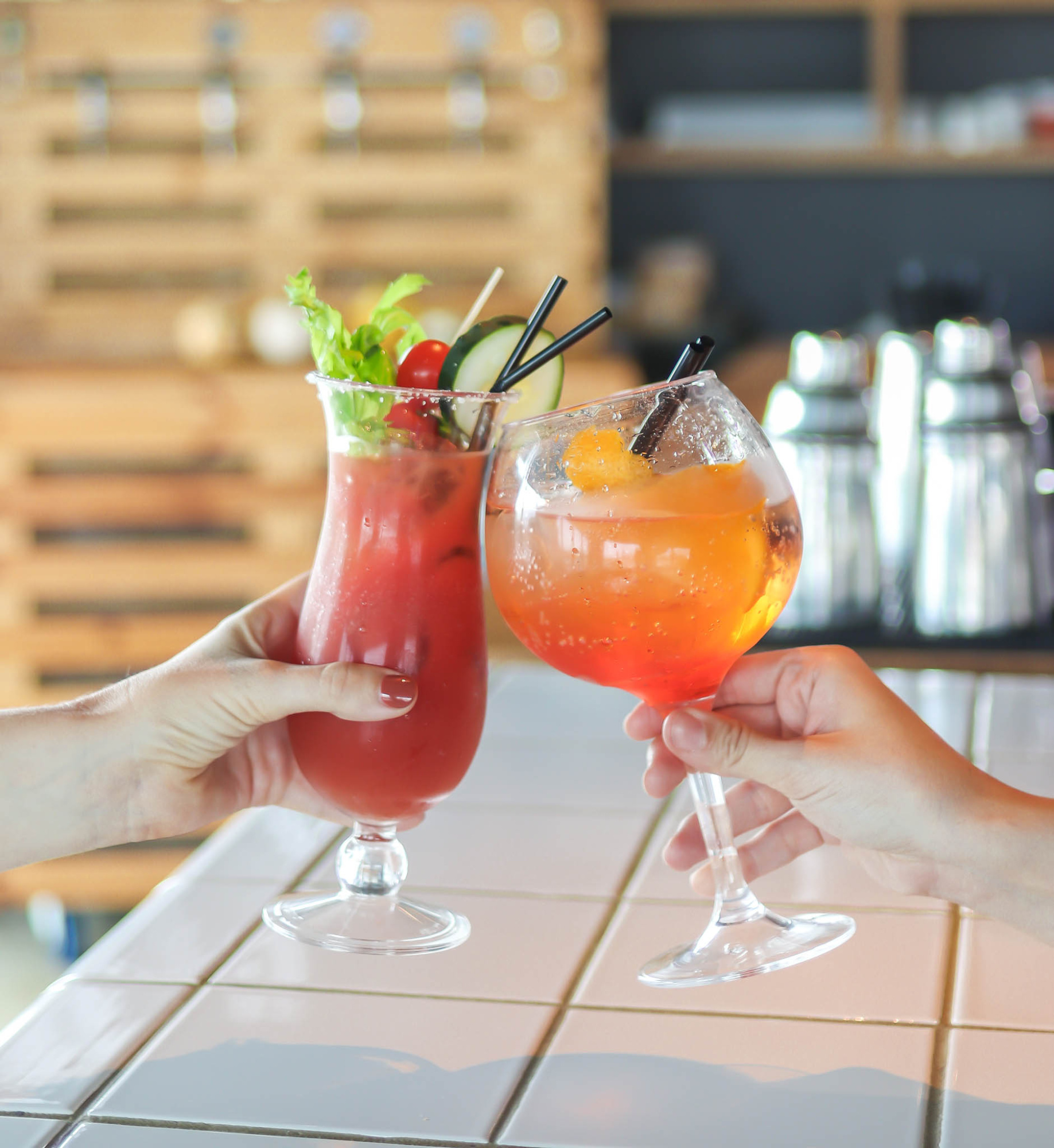 Dos manos brindan con dos cócteles en copas de cristal sobre una mesa.