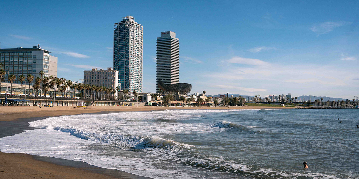 An urban beach with sand, waves, and buildings in the background is visible under a clear sky.