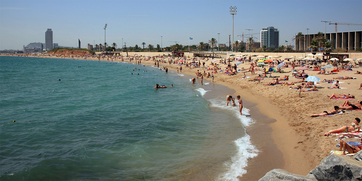 A sandy beach with bathers and the sea on the left can be seen under a clear sky.