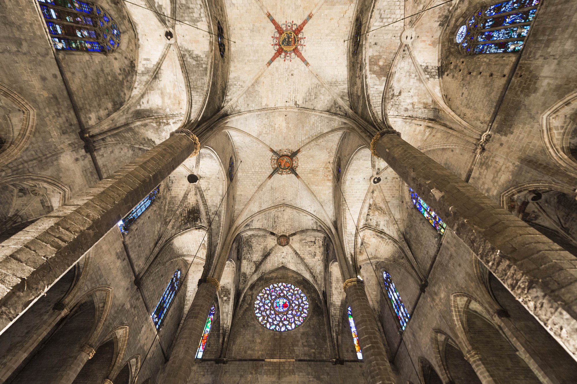 Vista interior de una iglesia con bóveda de piedra y vitrales en las ventanas.