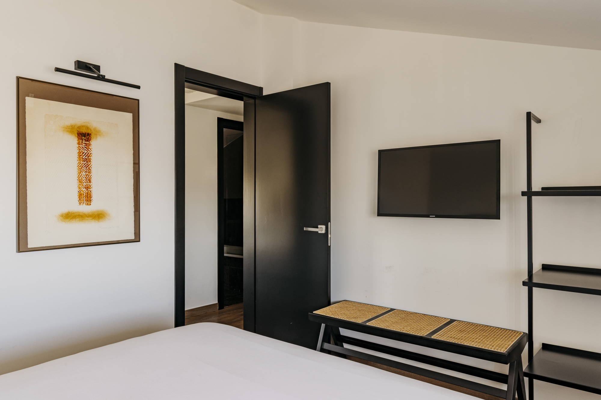 Una habitación de hotel moderna con decoración elegante y colores neutros, que incluye una cama grande, ropa de cama blanca y detalles decorativos en tonos suaves.