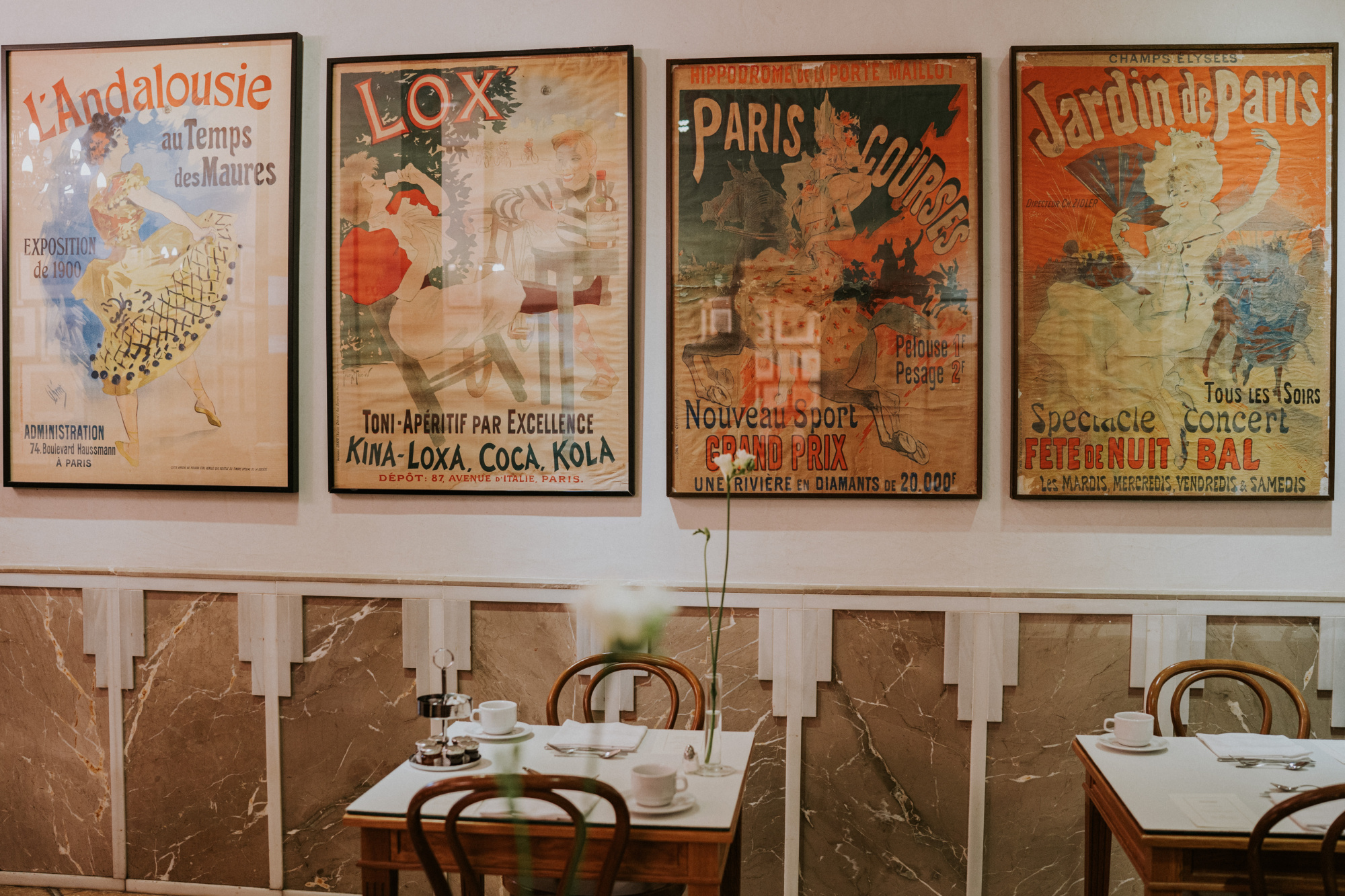 Se ven mesas con sillas y varios carteles enmarcados en una pared interior.