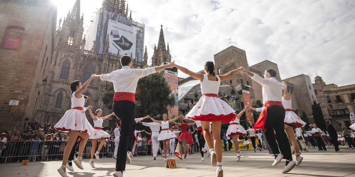 Un grupo de bailarines con vestidos blancos y rojos realiza una actuación en una plaza urbana.