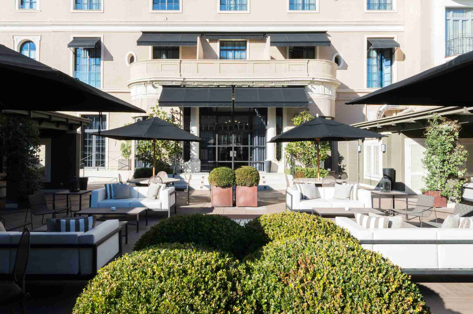 Se ve un patio interior con sofás, tumbonas y jardineras junto a una zona techada.