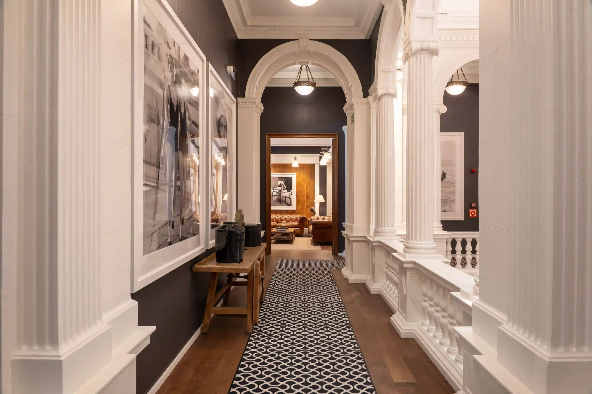 Indoor corridor with white columns, wooden benches and paintings on the walls.