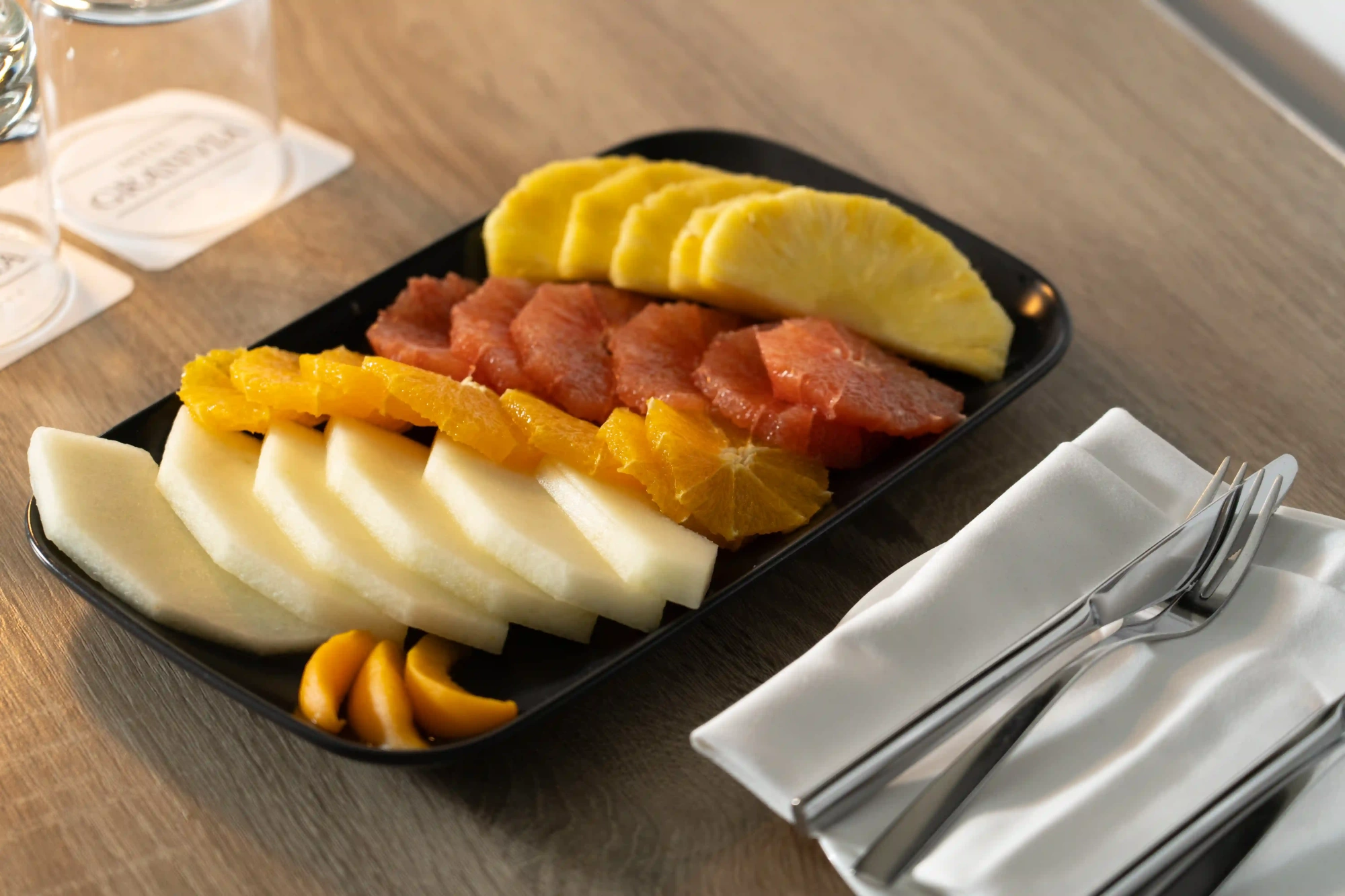 Se sirve fruta cortada en una bandeja negra sobre una mesa de madera.