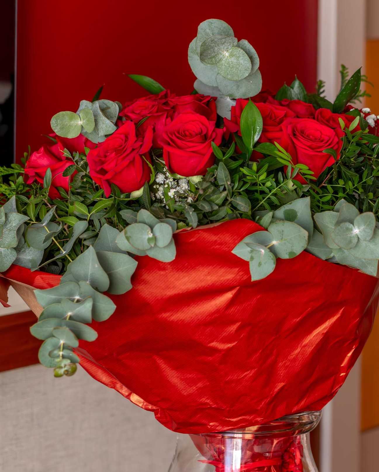 Se ve un ramo de rosas rojas y flores blancas sobre una mesa con tela roja.