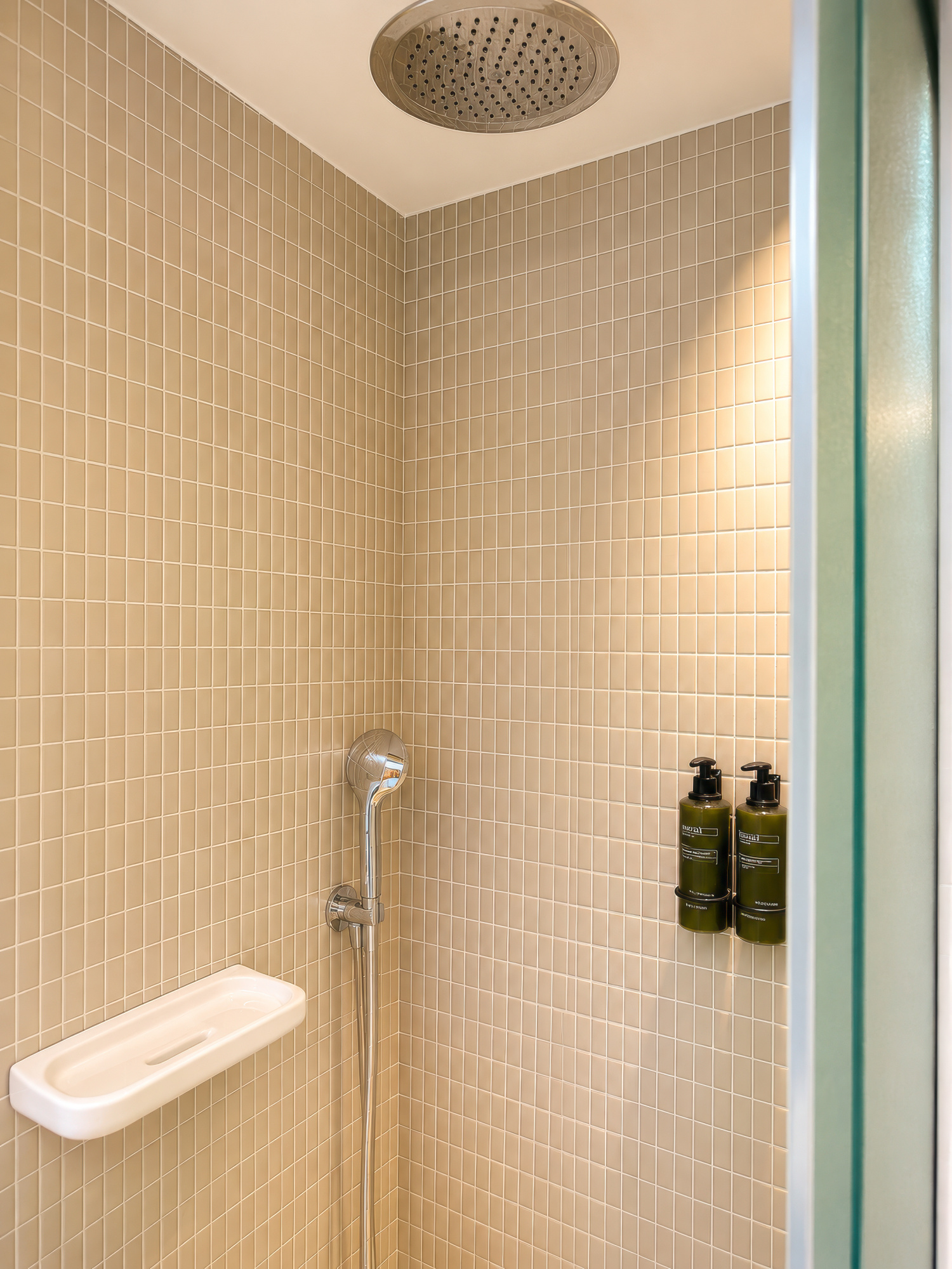 La imagen muestra una ducha con cabezal de lluvia, pared revestida y dispensadores en el interior del baño.