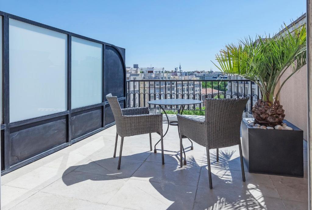 Terraza con mesa redonda, sillas de mimbre y una jardinera con palmera junto a una pared