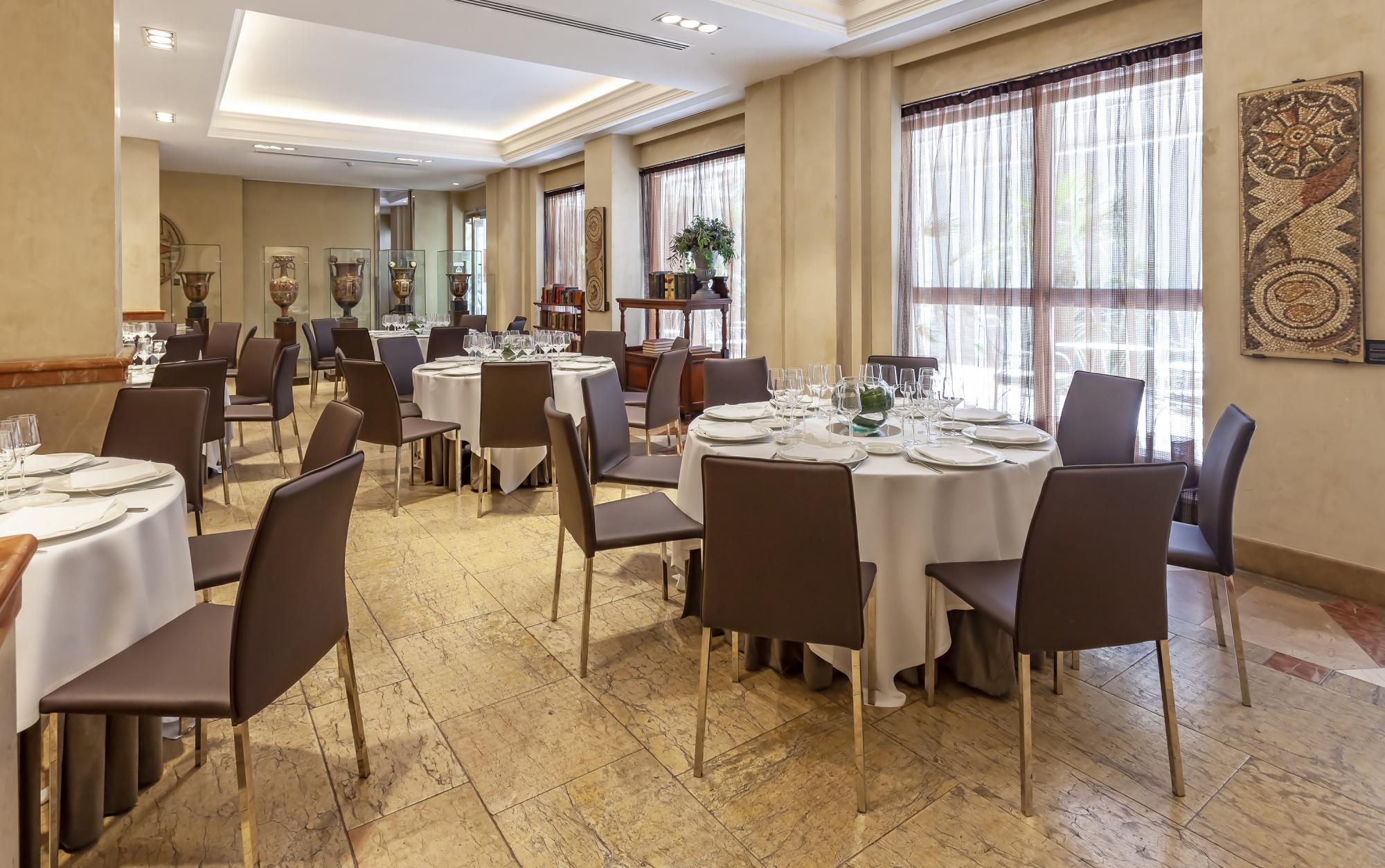 Se ve un comedor de banquete con mesas cubiertas, sillas y ventanas con cortinas.