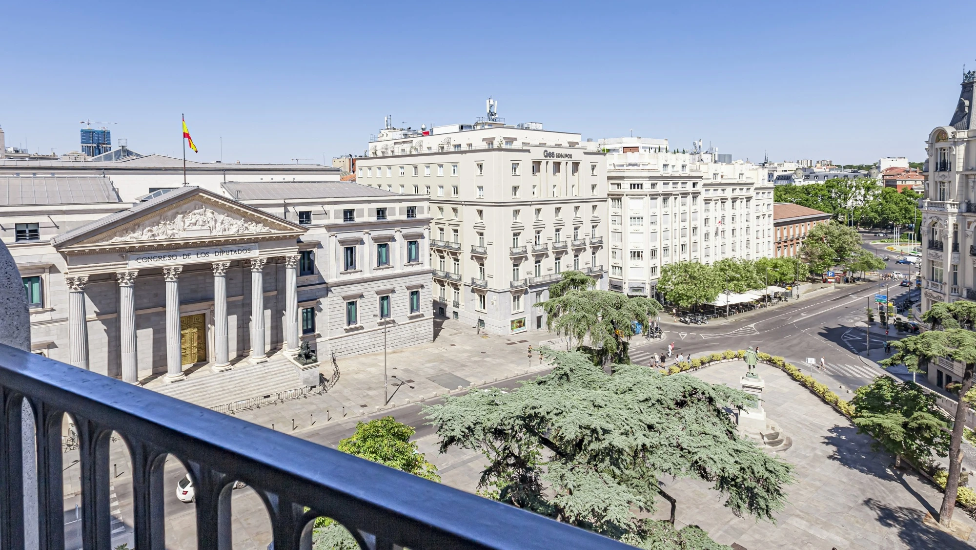 Se ve un balcón con barandilla y una vista de edificios y calles en la ciudad.