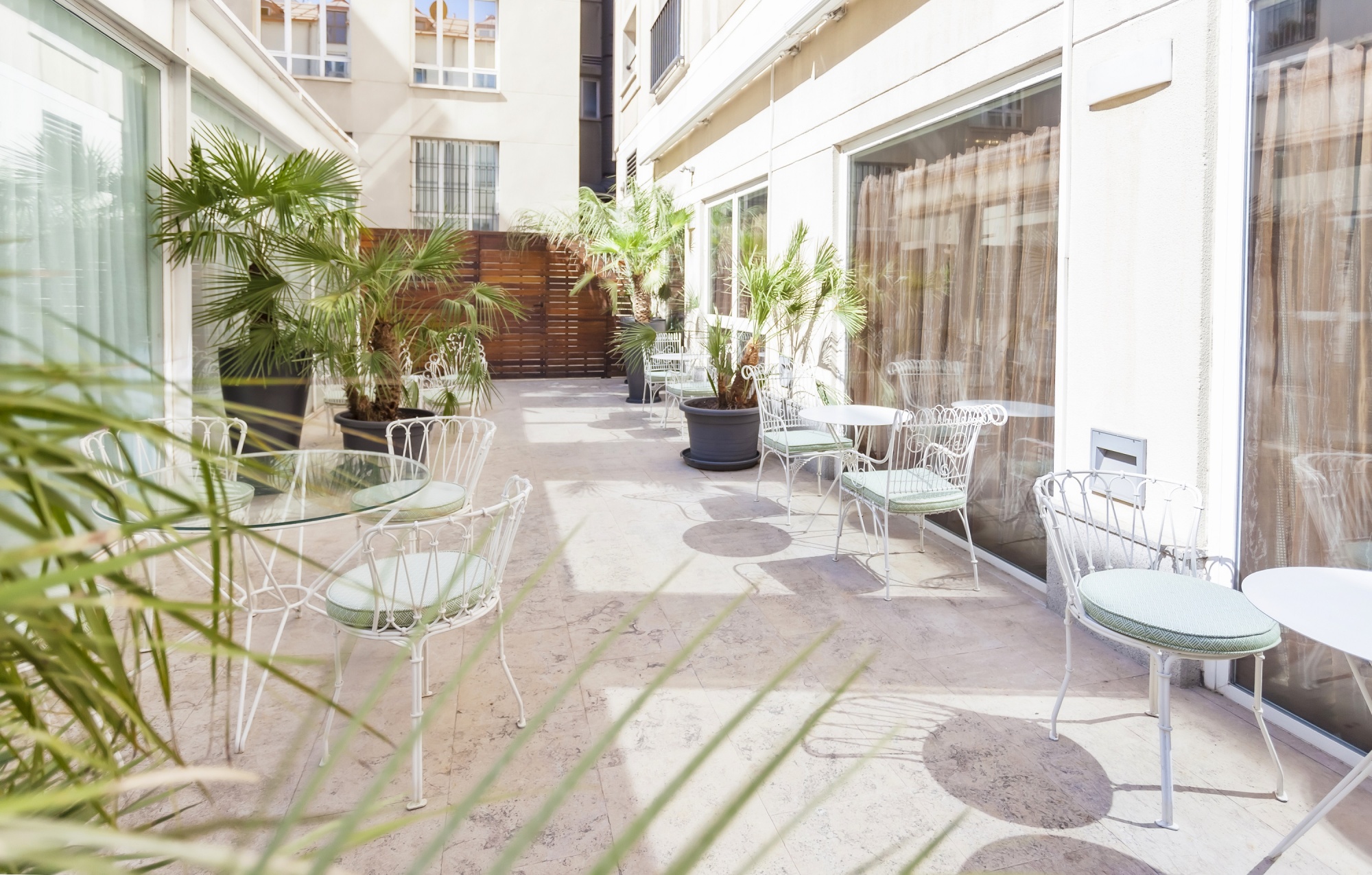 Se ve un patio interior con mesas y sillas de exterior, plantas en macetas y suelo de baldosas.