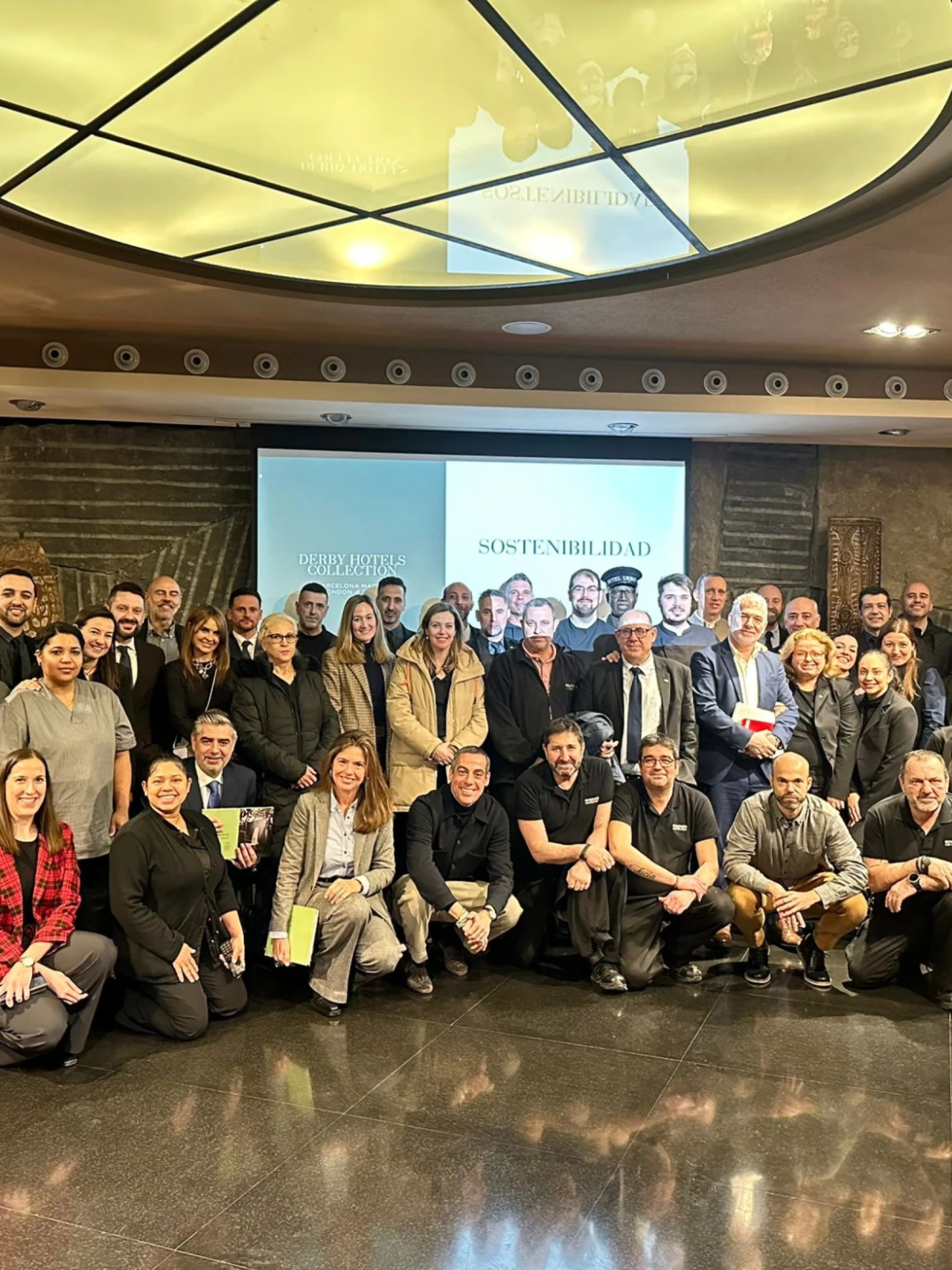 Un grupo de personas posa en una sala con pantalla y techo con iluminación circular.