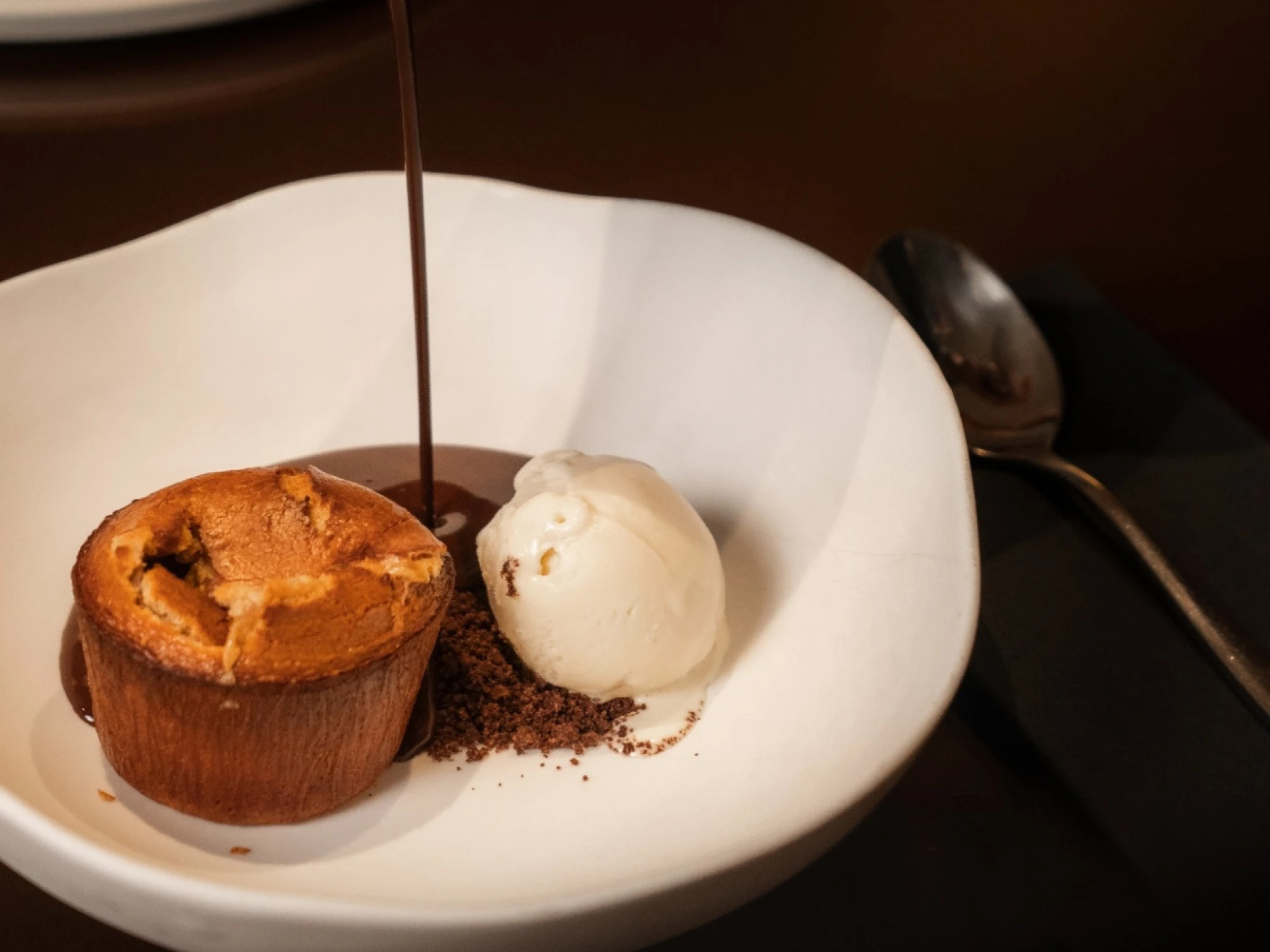 Se ve un postre servido en un plato blanco con una bola de helado y un polvo oscuro encima.
