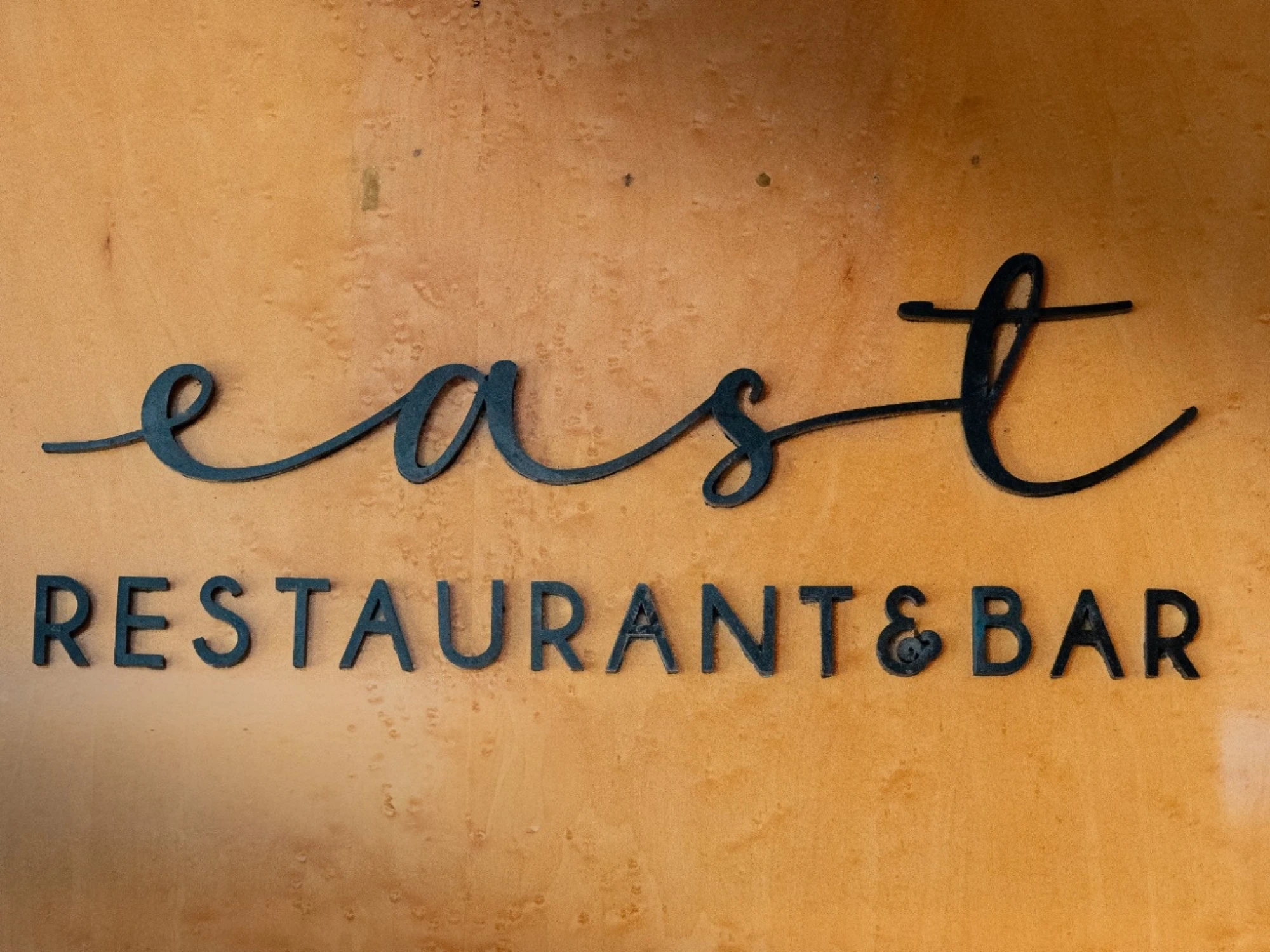Se ve un letrero con el texto “east restaurant & bar” sobre una pared.