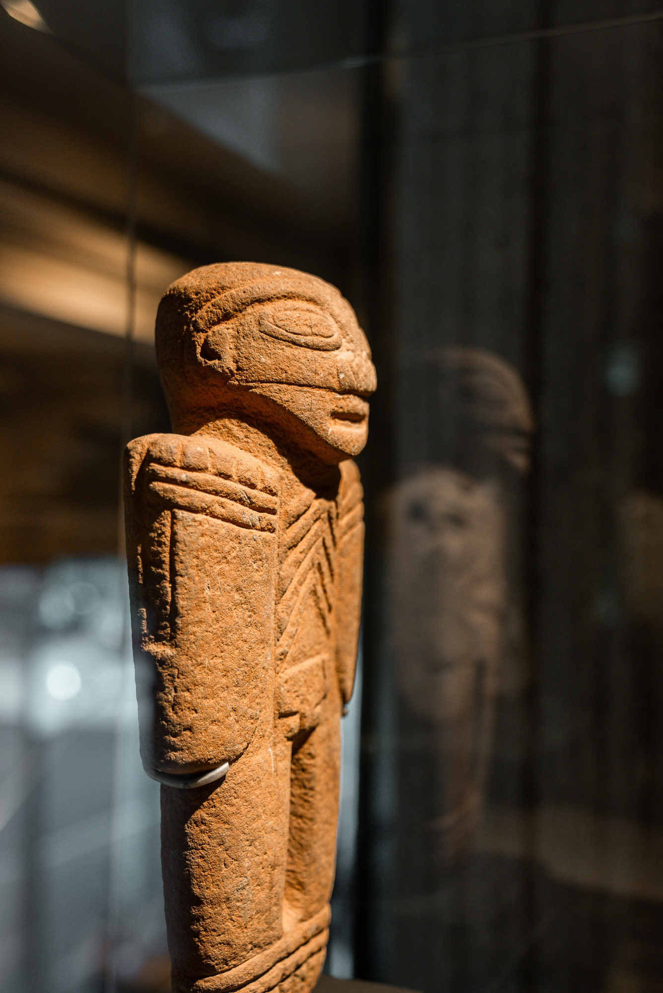 Se ve una escultura de piedra precolombina dentro de una vitrina con otras piezas al fondo.