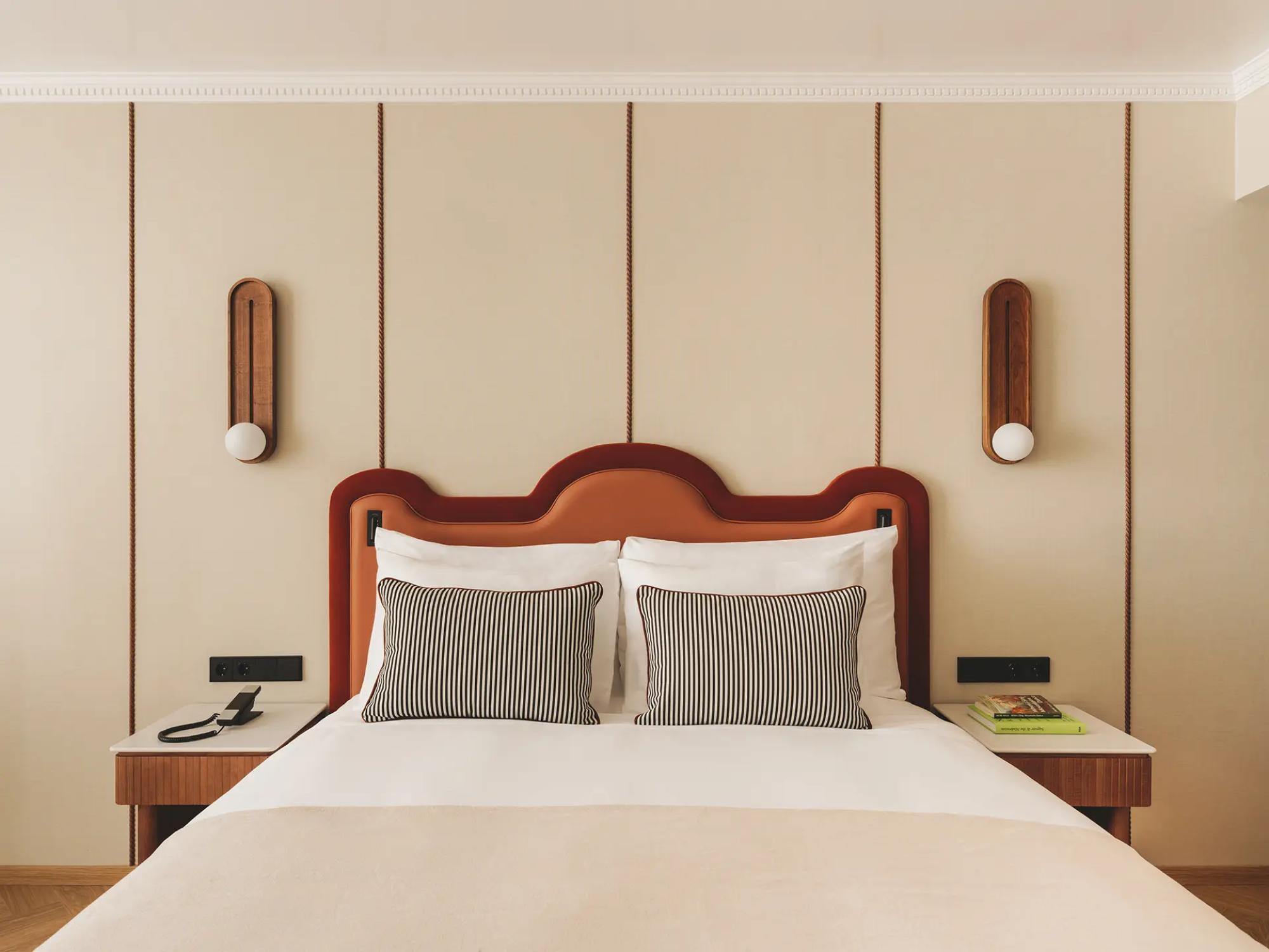 Se ve una cama con cabecero de madera, dos mesitas y lámparas de pared en un dormitorio.
